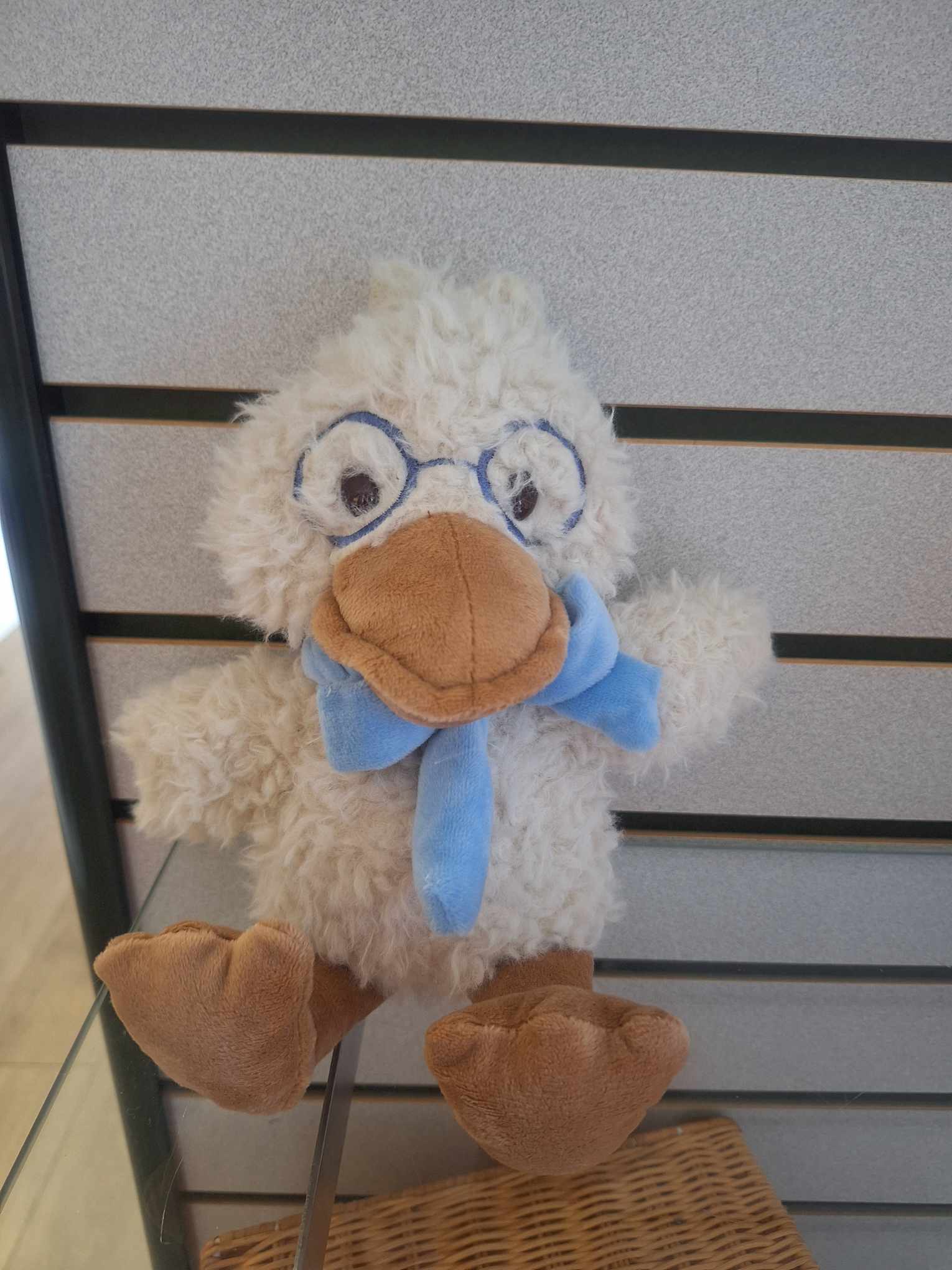 Plush duck toy with fuzzy cream fur, blue scarf, and fabric glasses on a display shelf
