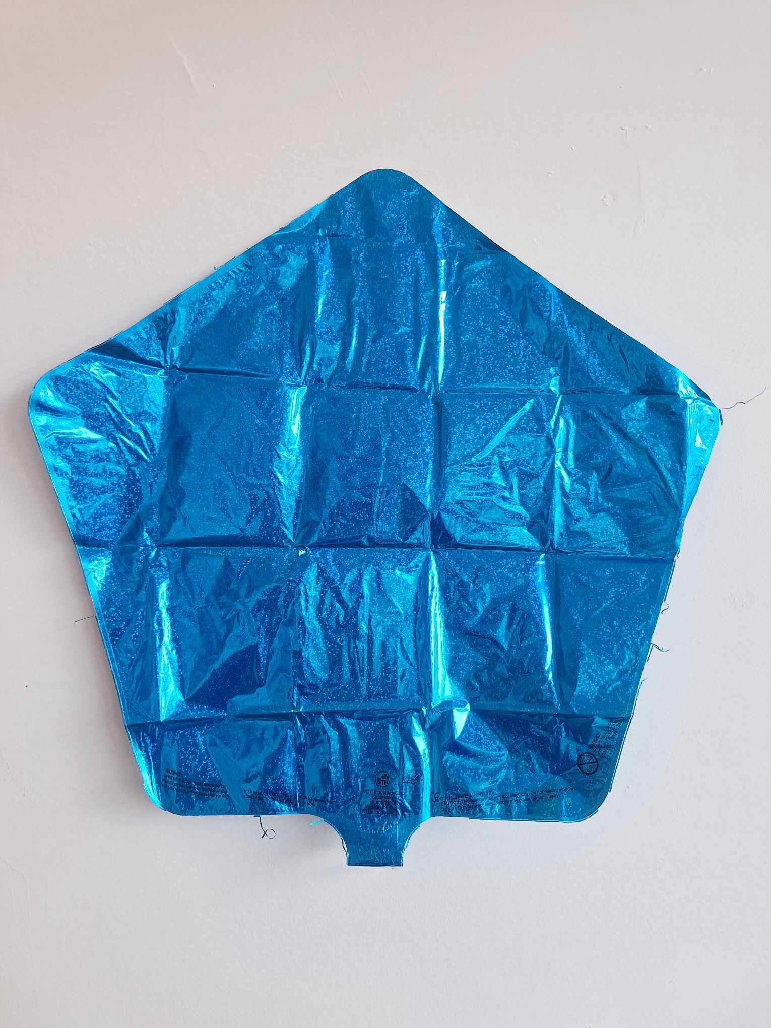 Blue metallic pentagon-shaped foil balloon against a white wall