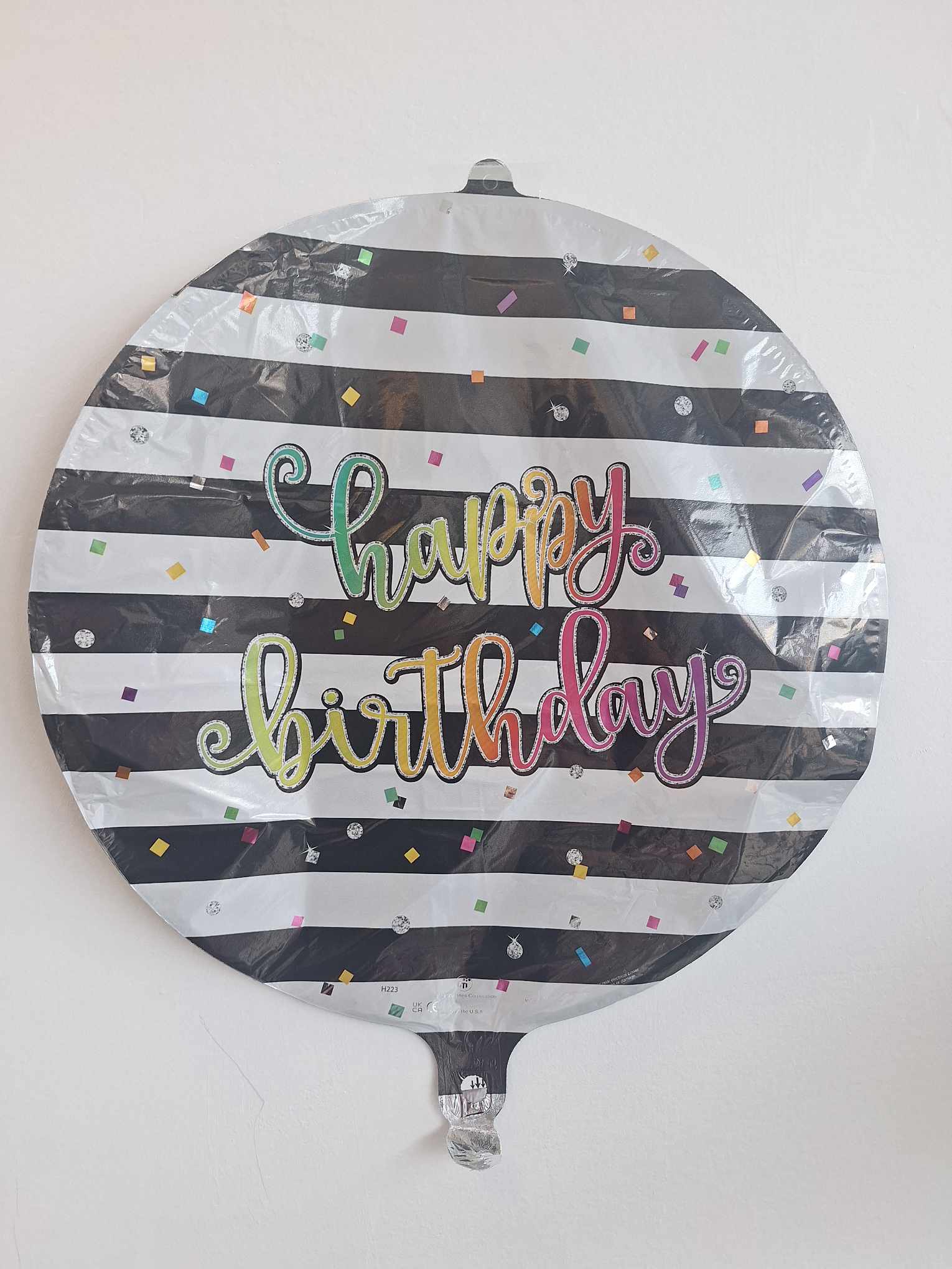 Round birthday balloon with black-and-white stripes and colorful confetti text