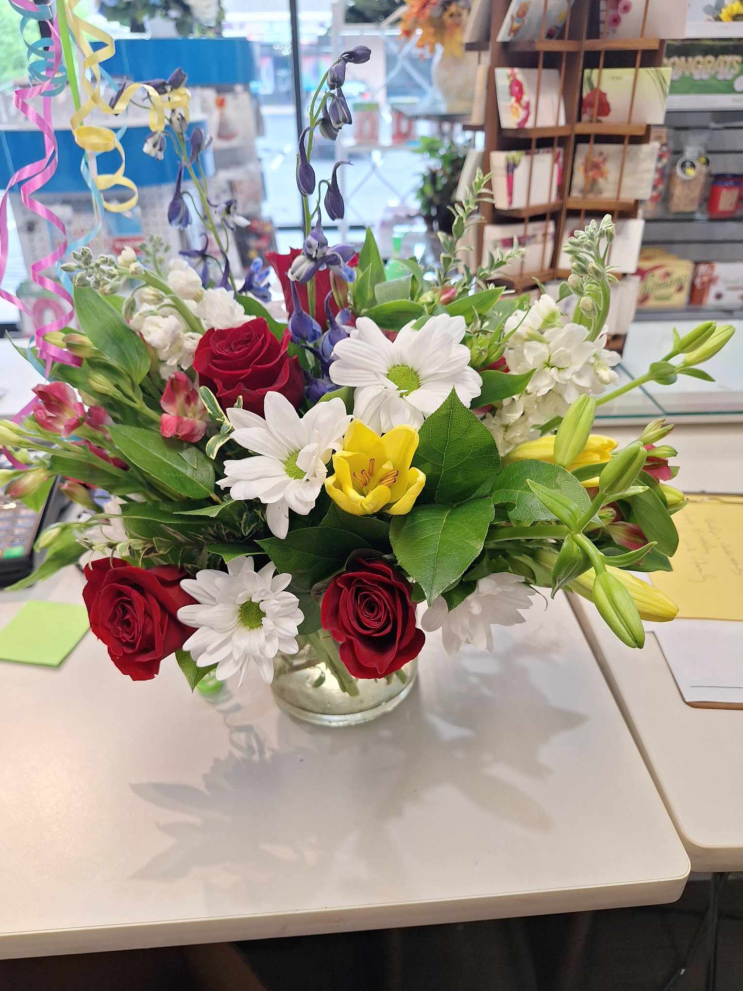 Mixed bouquet of red roses, white daisies, and yellow lilies in a glass vase