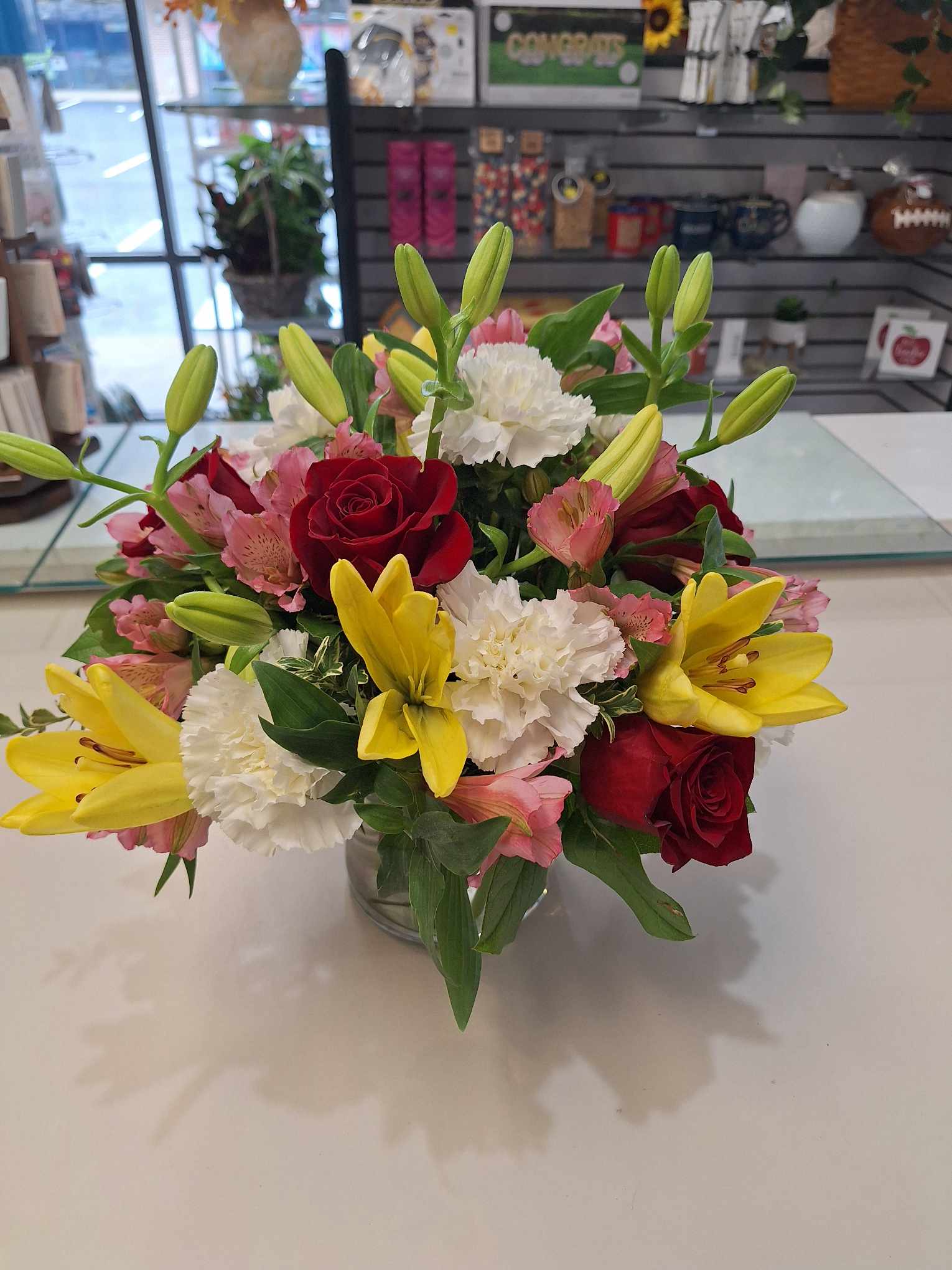 Bouquet of red roses, yellow lilies, and white carnations in a glass vase
