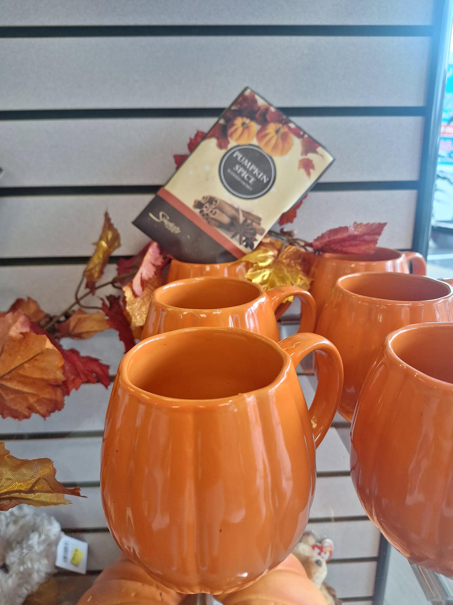 Orange pumpkin-shaped mugs displayed with autumn leaf decor