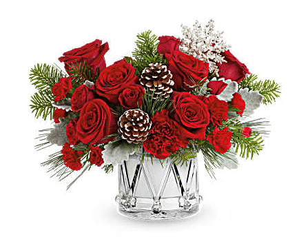 Red roses arranged in a clear glass vase with pinecones and winter greenery