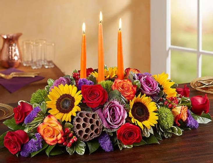 Low floral centerpiece with lit orange candles and sunflowers