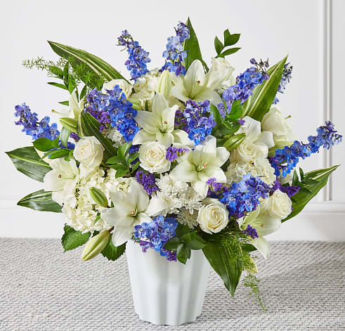 White lilies and roses with blue flowers in a white vase