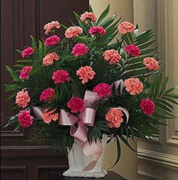 Pink and coral carnations in a white vase with a pink ribbon