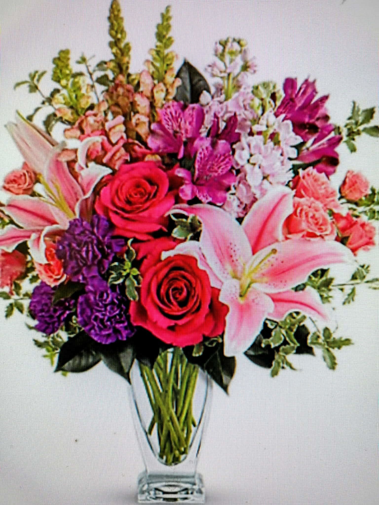 Mixed bouquet of pink lilies, roses, and purple flowers in a clear vase