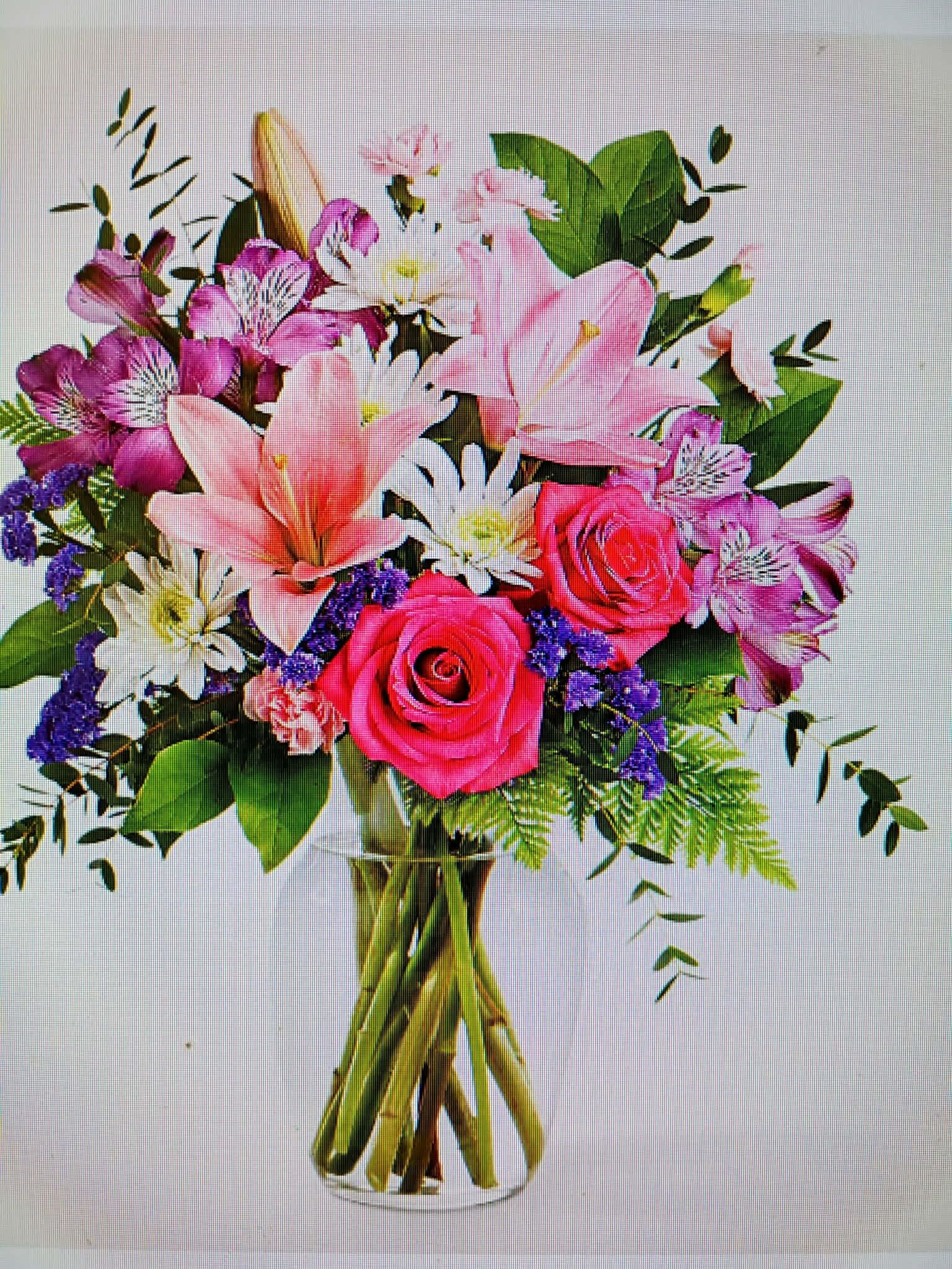 Mixed bouquet of pink roses, lilies, and purple flowers in a glass vase