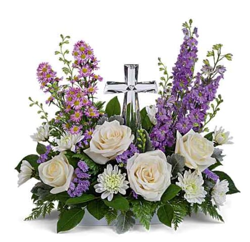 White roses and purple flowers arranged around a clear glass cross