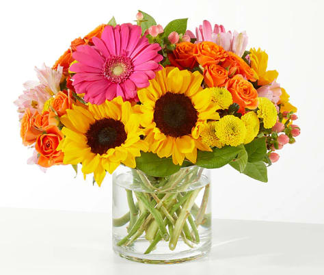 Bright mixed bouquet with sunflowers, roses, and a pink gerbera in a glass vase