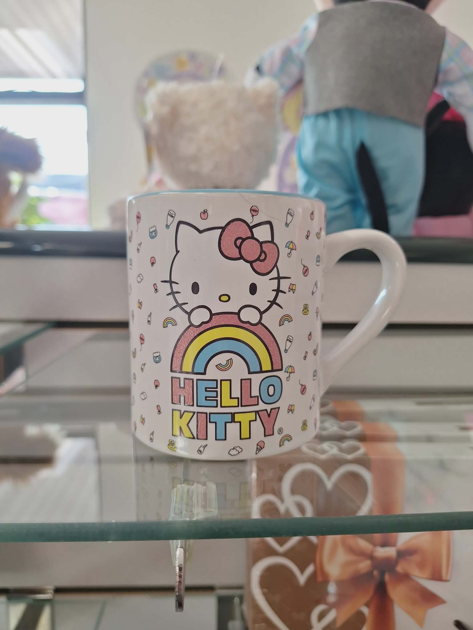 Hello Kitty mug with a rainbow graphic on a glass shelf