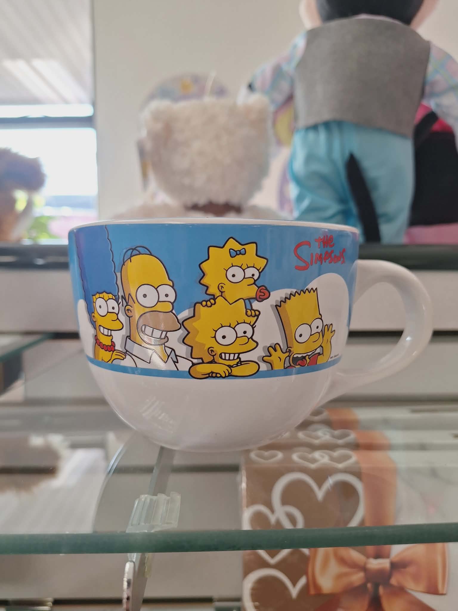 The Simpsons mug with a white handle on a glass shelf