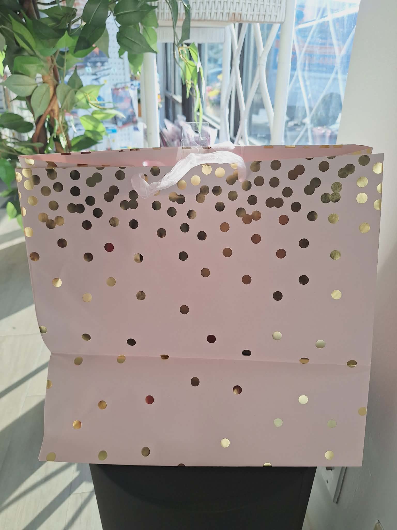 Pink gift bag with gold polka dots and white ribbon handles