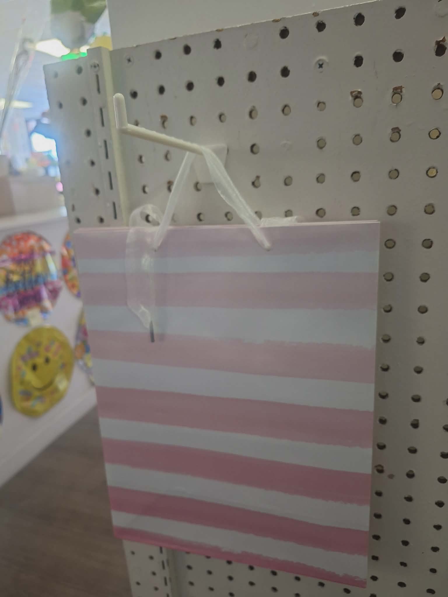 Pink and white striped gift bag hanging on a pegboard display