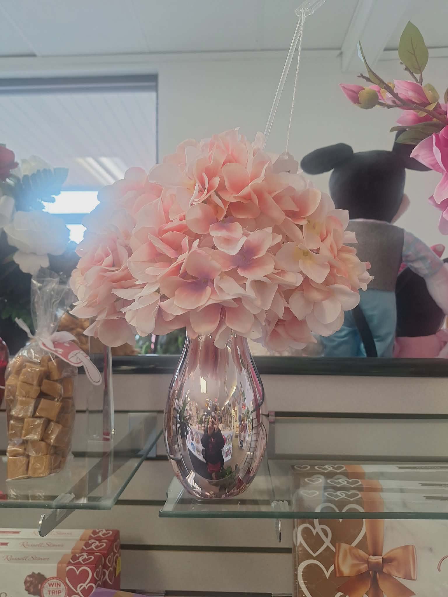 Pink hydrangea bouquet in a reflective vase on a glass shelf