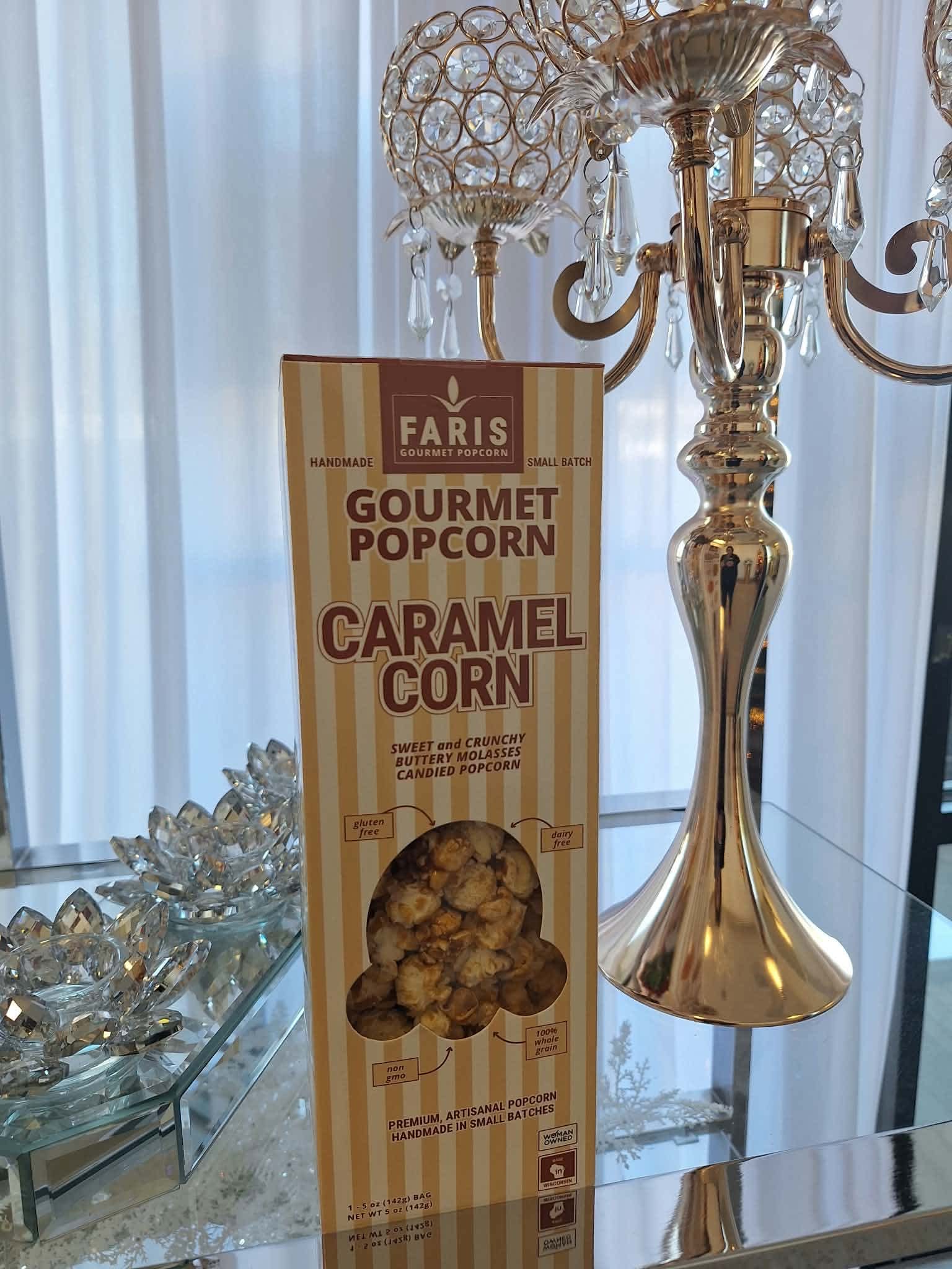 Box of caramel gourmet popcorn on a mirrored table beside a gold candelabra
