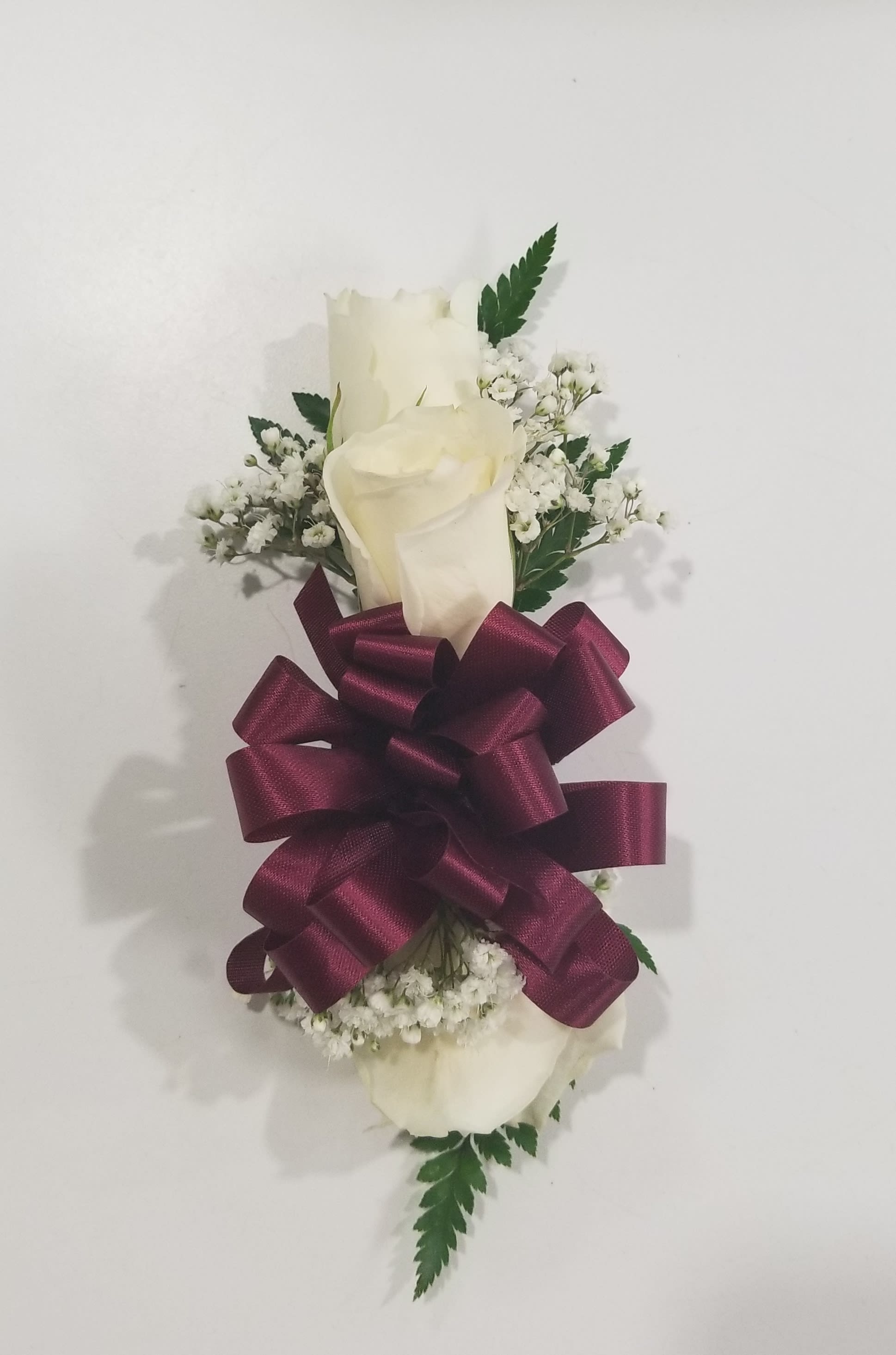 White rose corsage with baby's breath and a burgundy ribbon