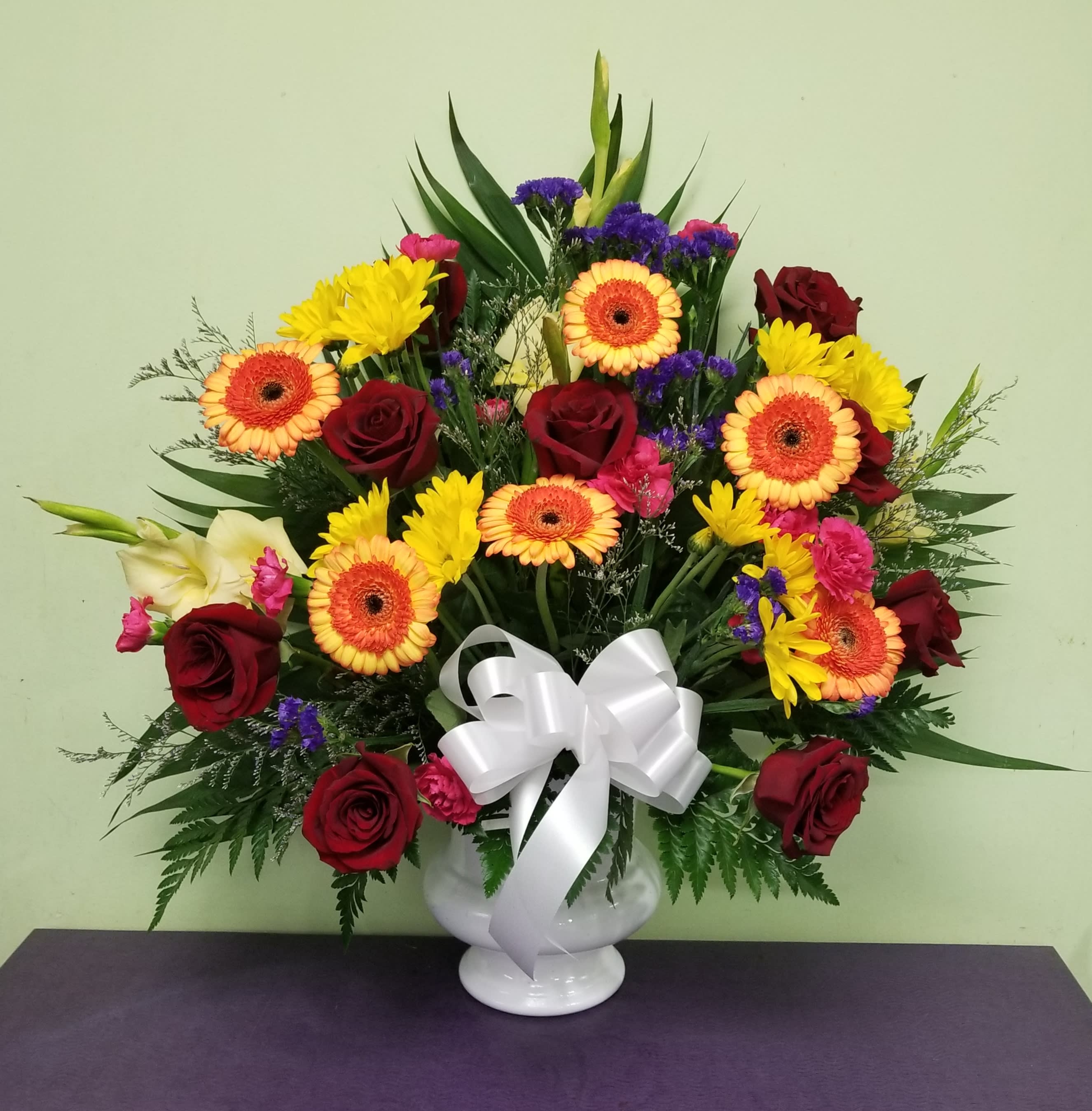 Mixed bouquet of red roses, yellow daisies, and orange gerberas in a white vase