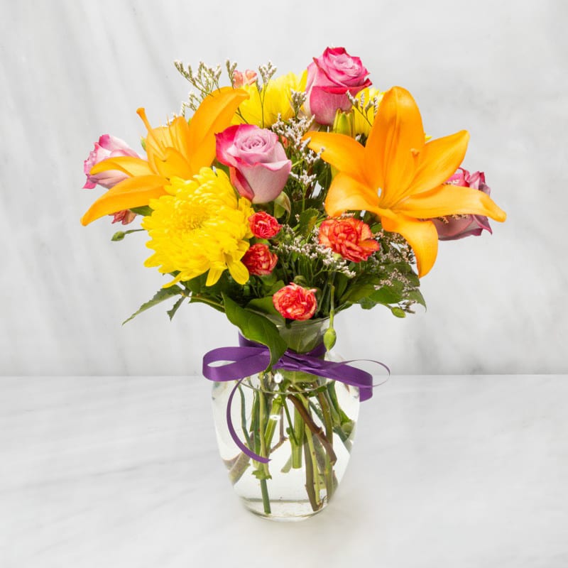 Bouquet of orange lilies, pink roses, and yellow mums in a glass vase