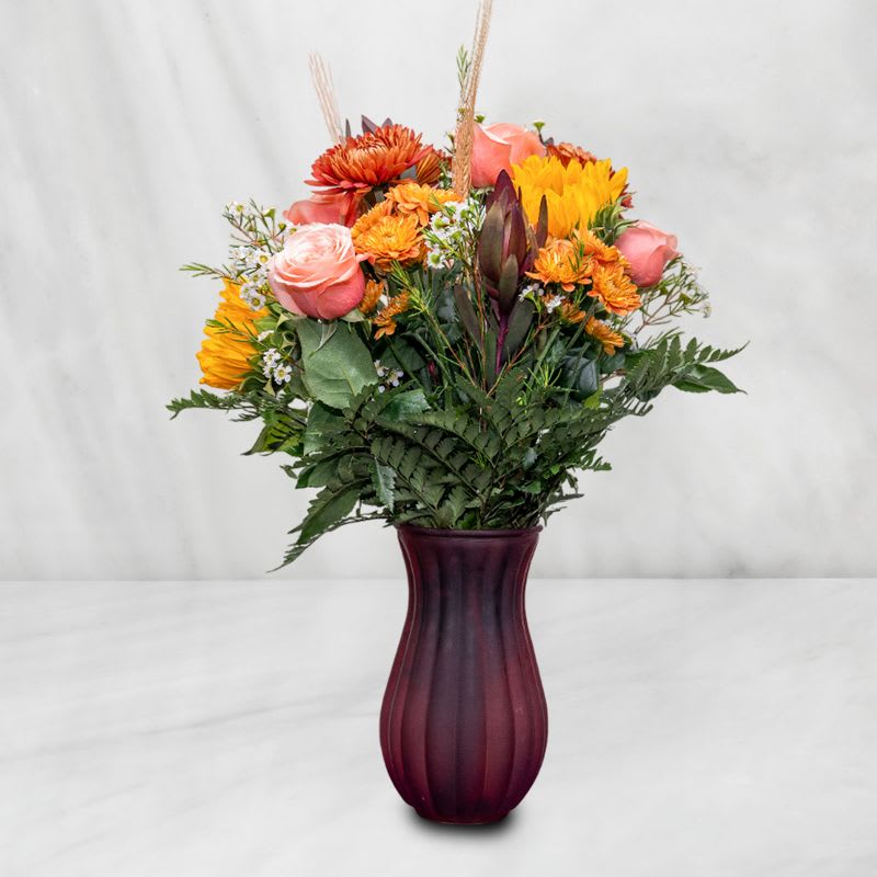 Mixed bouquet of pink, orange, and yellow flowers in a purple vase