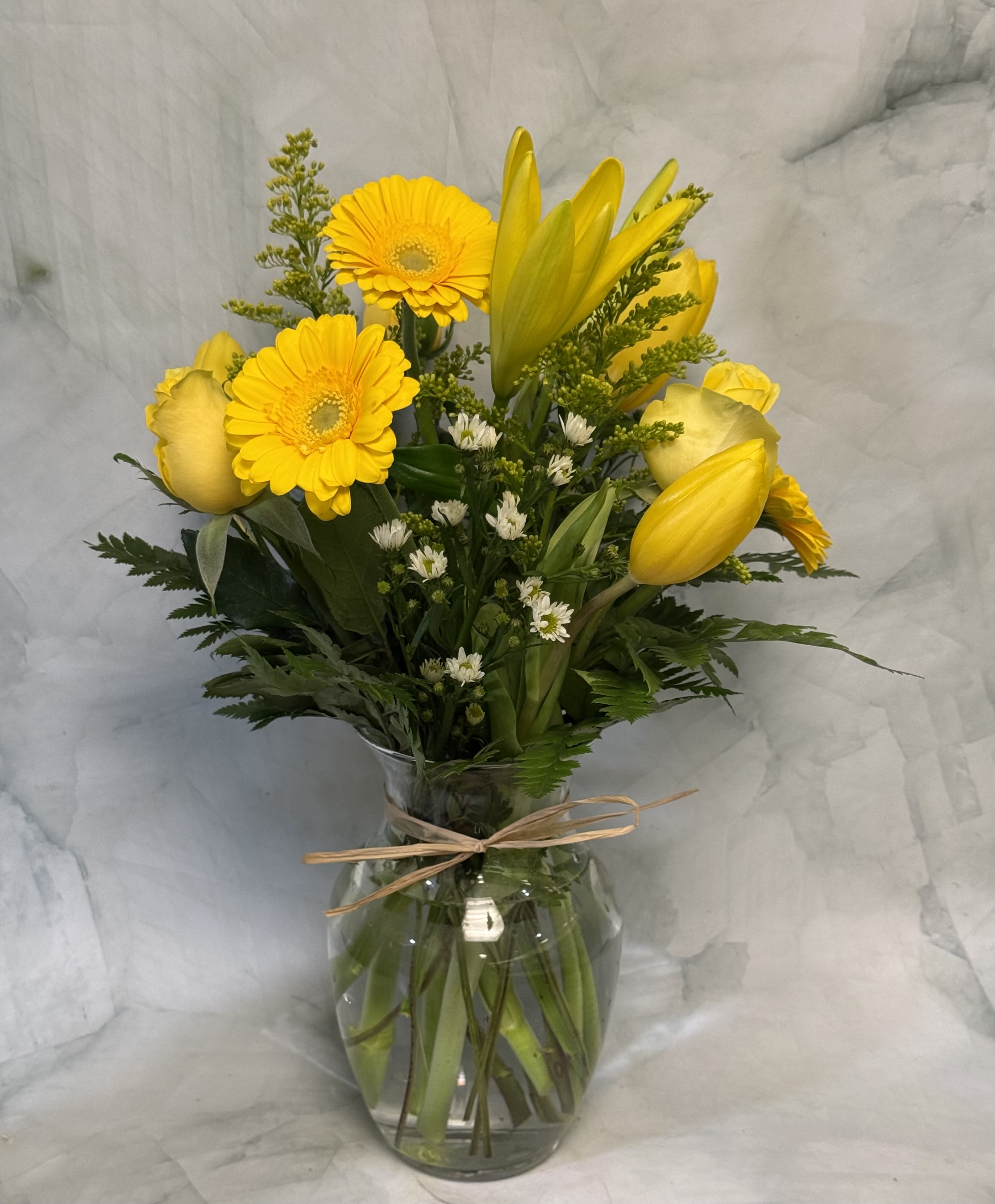 Yellow flowers arranged in a clear glass vase with a ribbon tie.