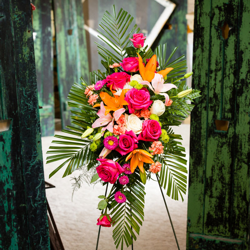 Standing floral spray with pink roses, lilies, and palm fronds