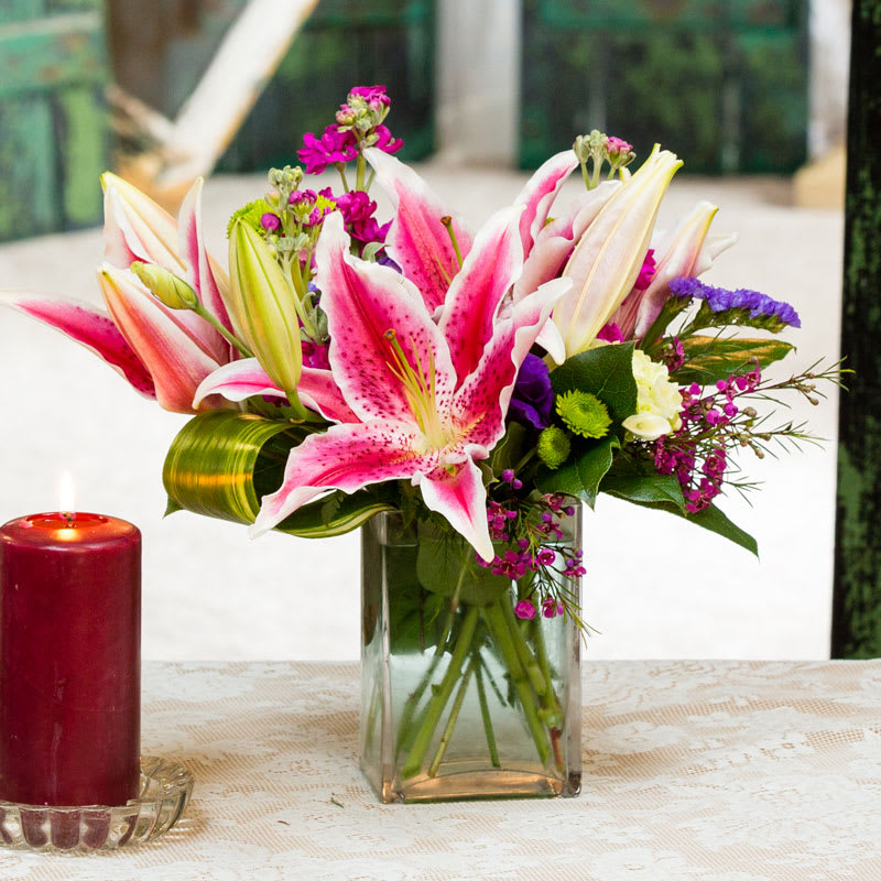 Pink and white lilies arranged in a clear glass vase beside a red candle