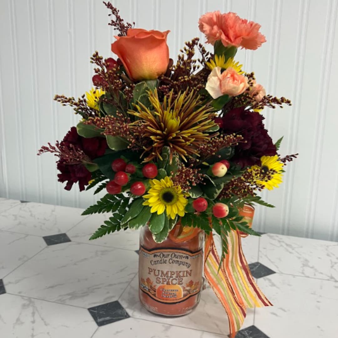 Mixed bouquet in a pumpkin spice candle jar with a striped ribbon