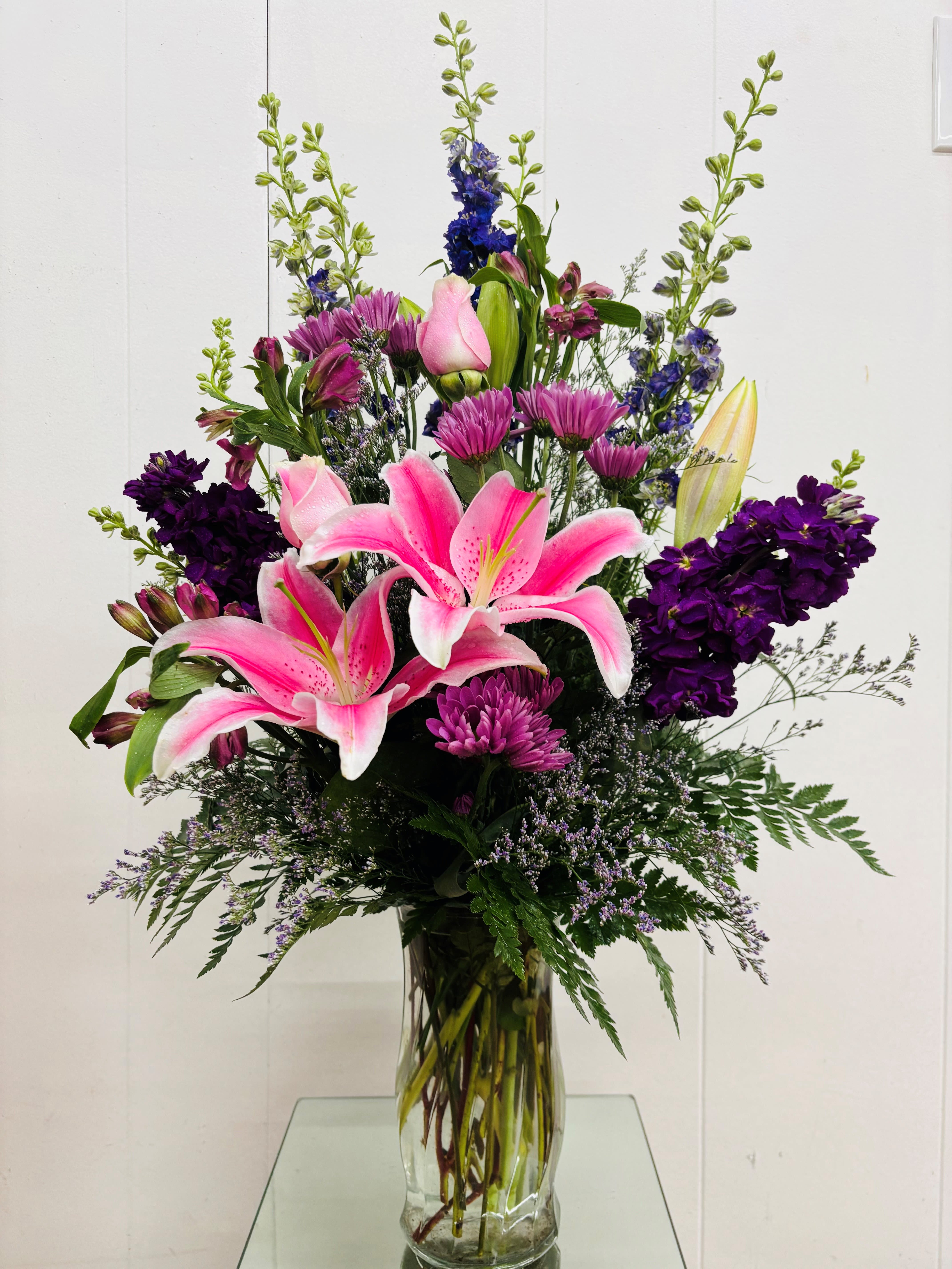 Pink lilies and purple flowers arranged in a clear glass vase