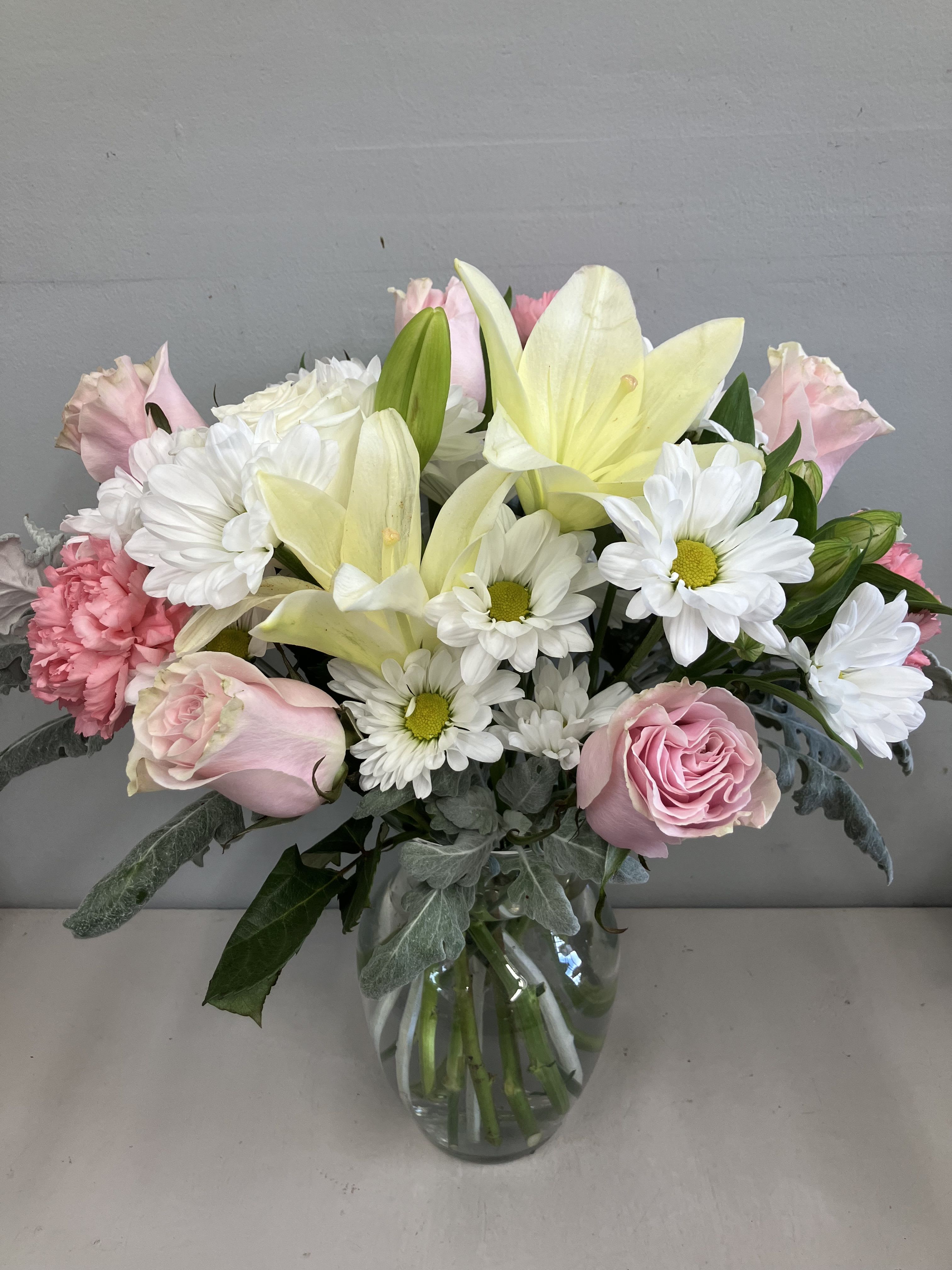 Pink roses, white daisies, and pale yellow lilies in a glass vase
