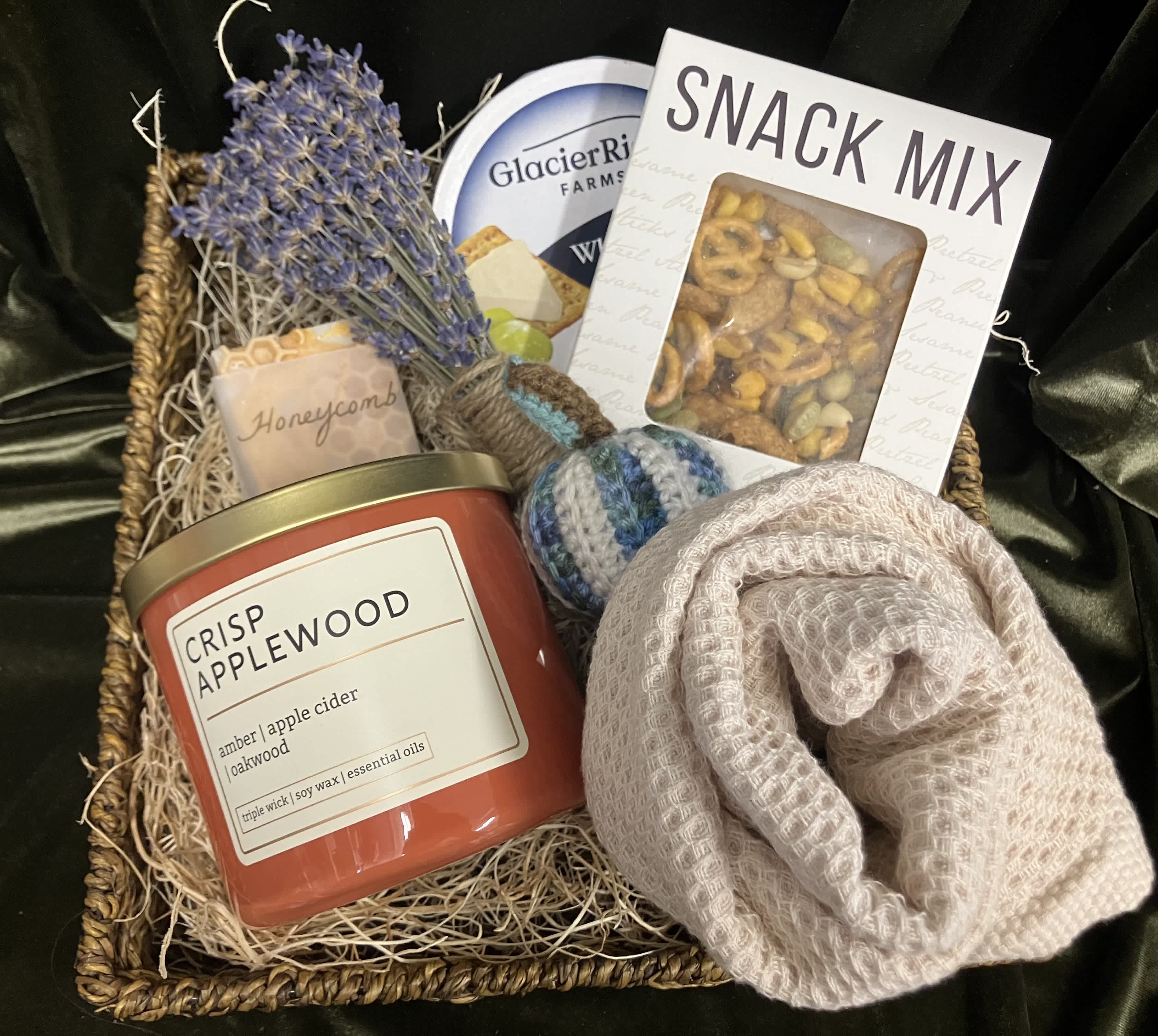 Gift basket with a candle, snack mix, soap, and a rolled knit item