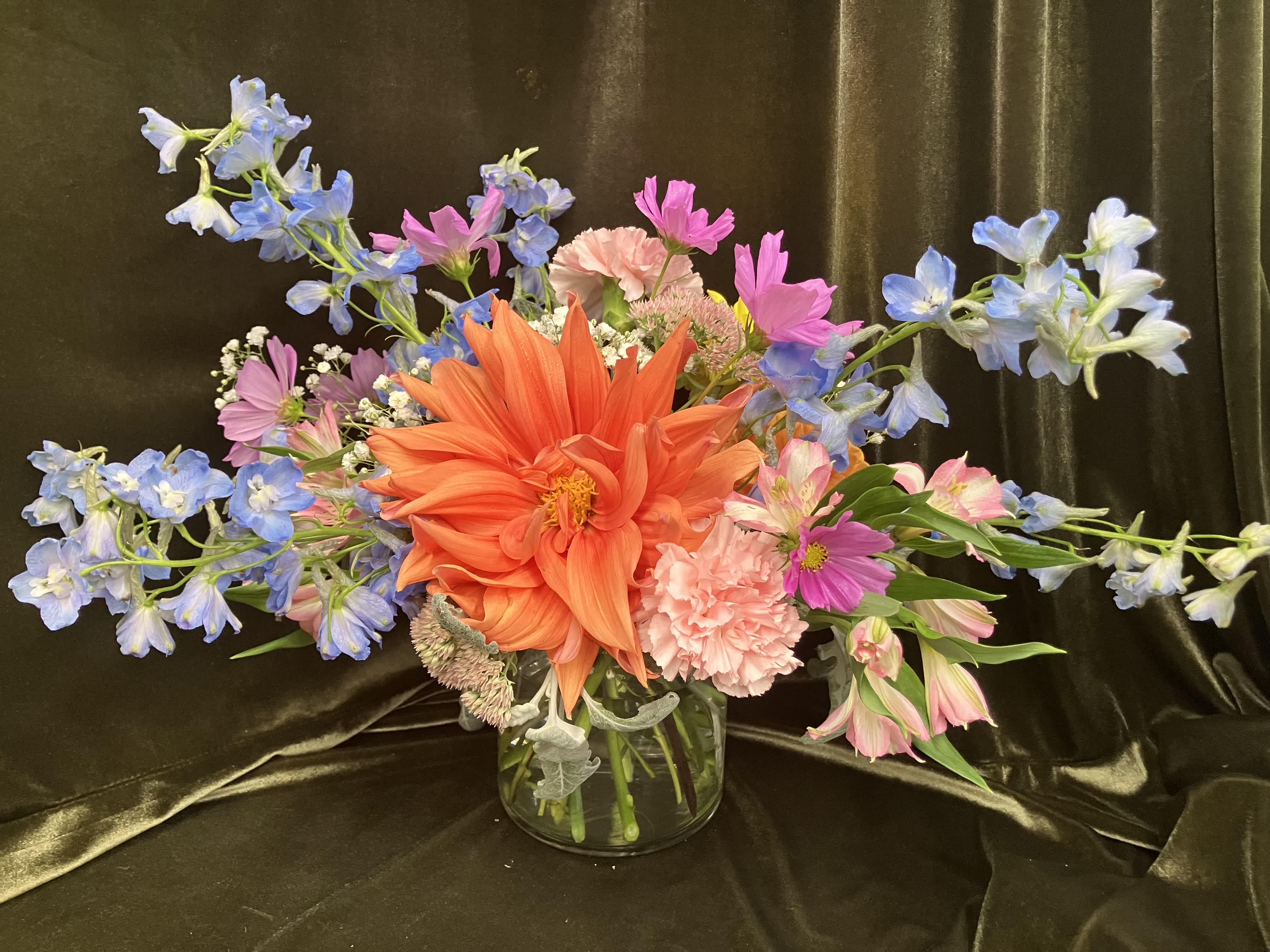 Colorful mixed bouquet in a clear glass vase with orange, pink, and blue flowers