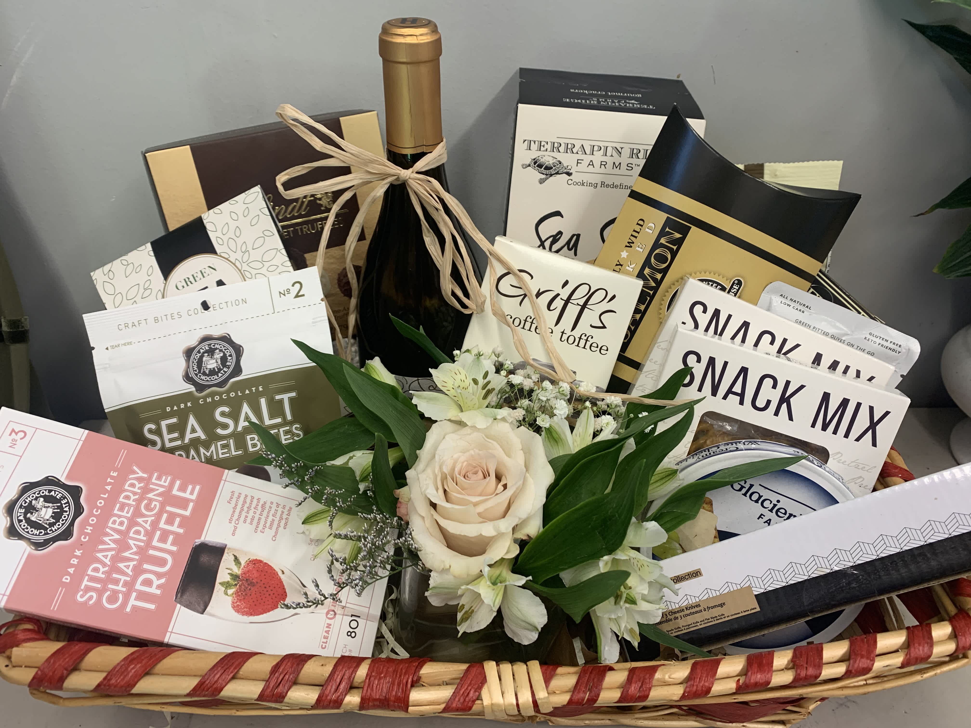 Gift basket with a small rose arrangement and assorted snacks, wine, and chocolates