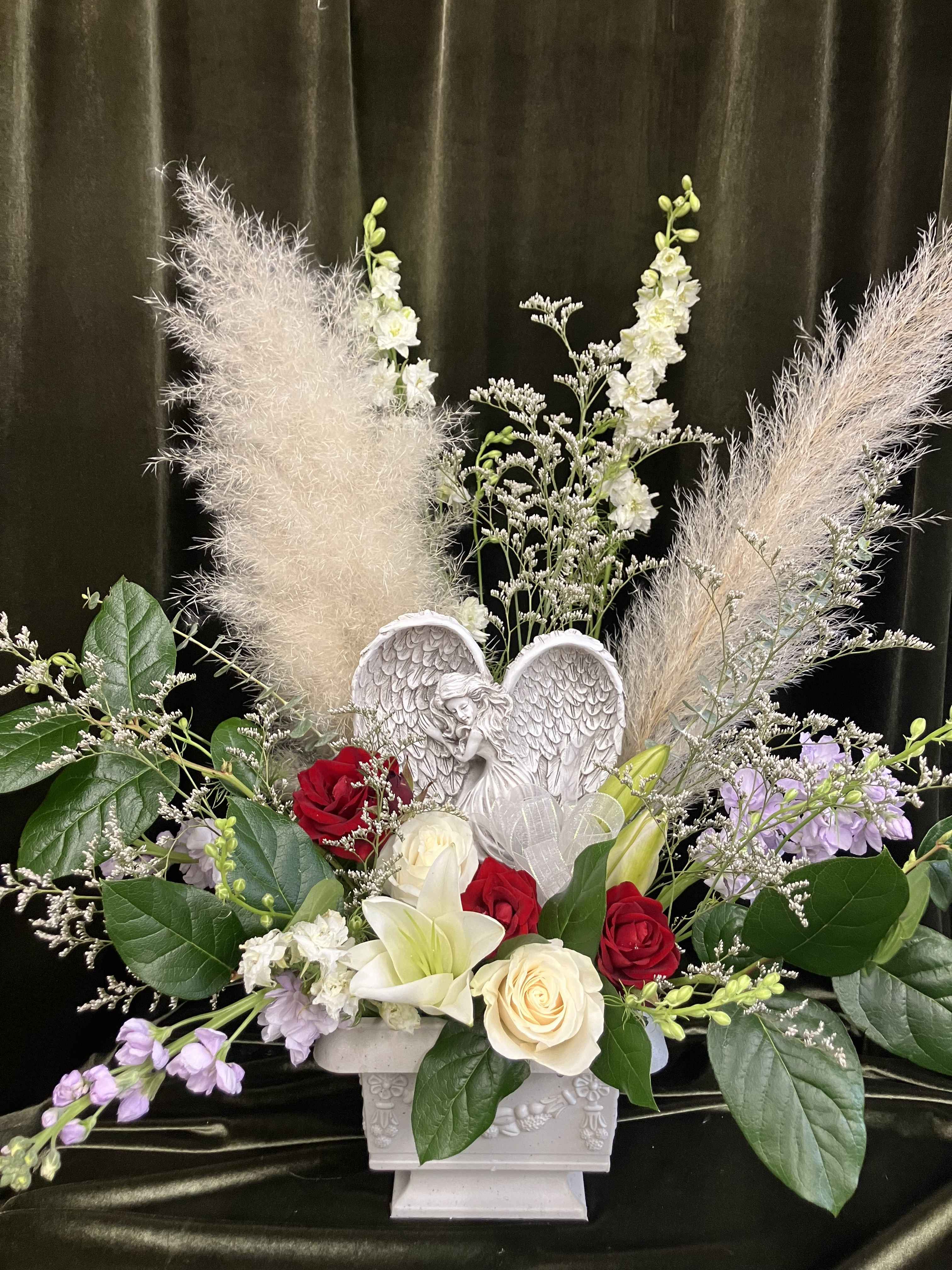 Mixed floral arrangement with roses, lilies, and an angel figurine in a white urn