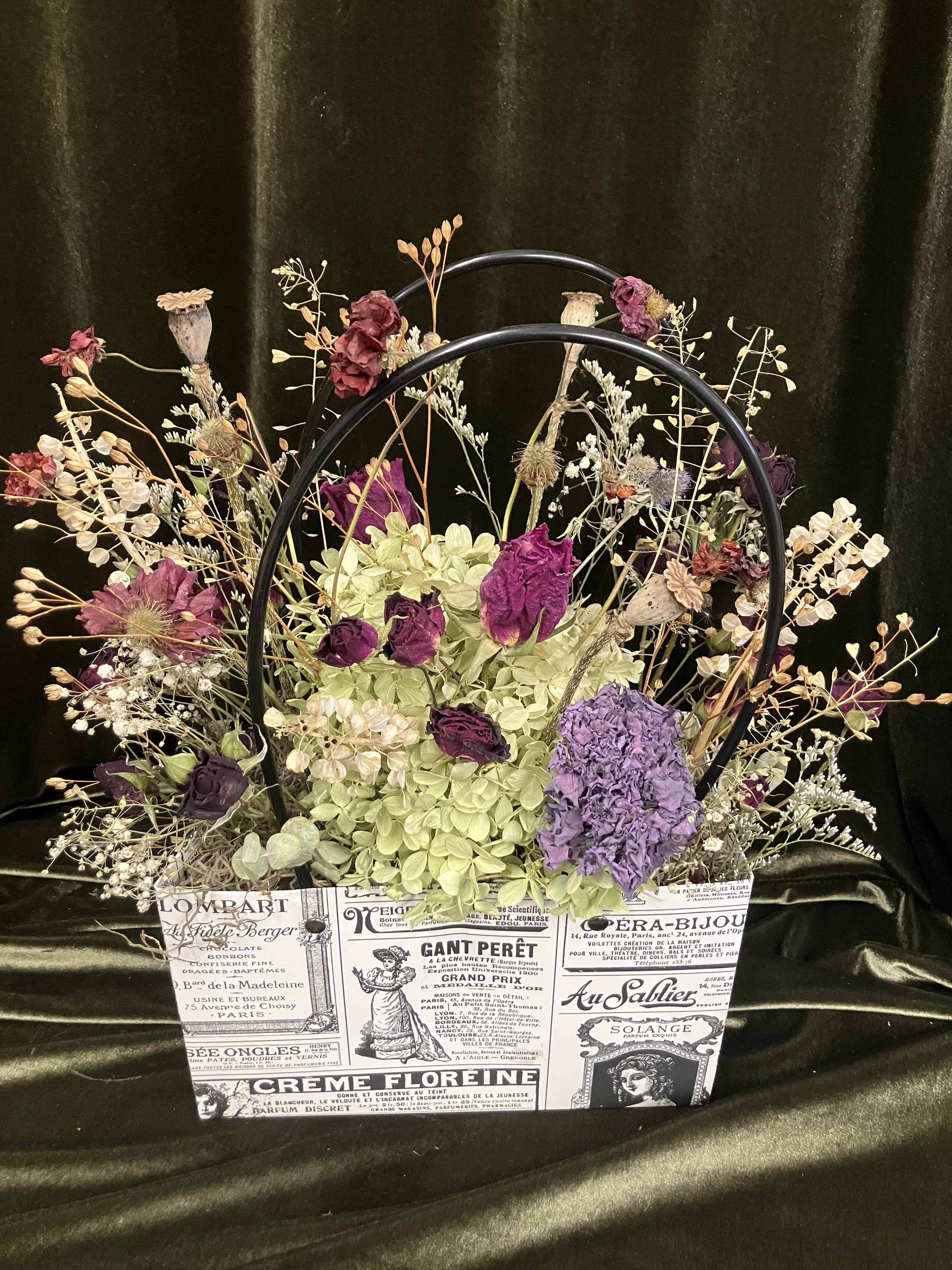 Dried floral arrangement in a printed paper bag with purple and cream blooms