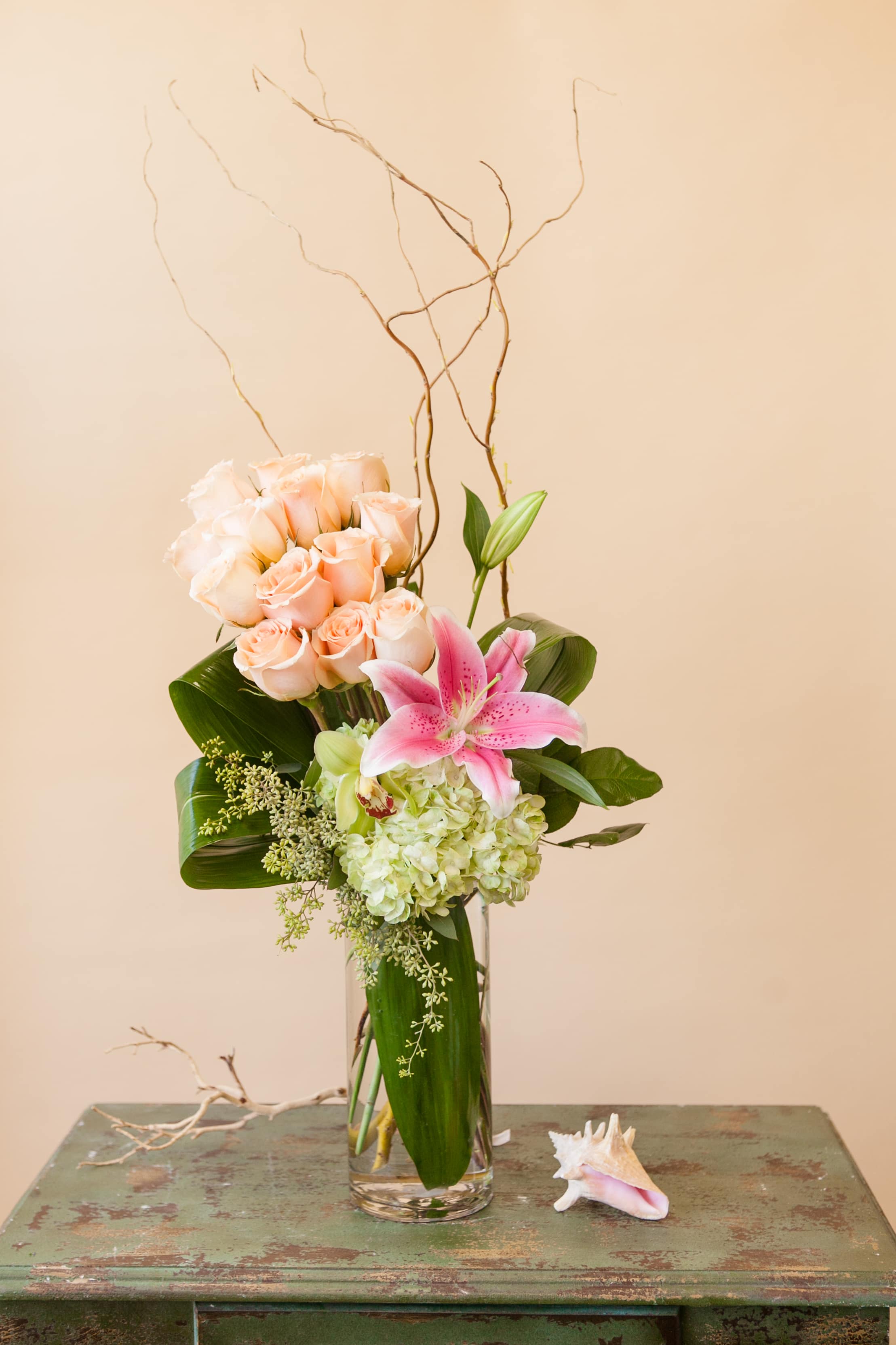 Tall bouquet of peach roses and pink lily in a glass vase