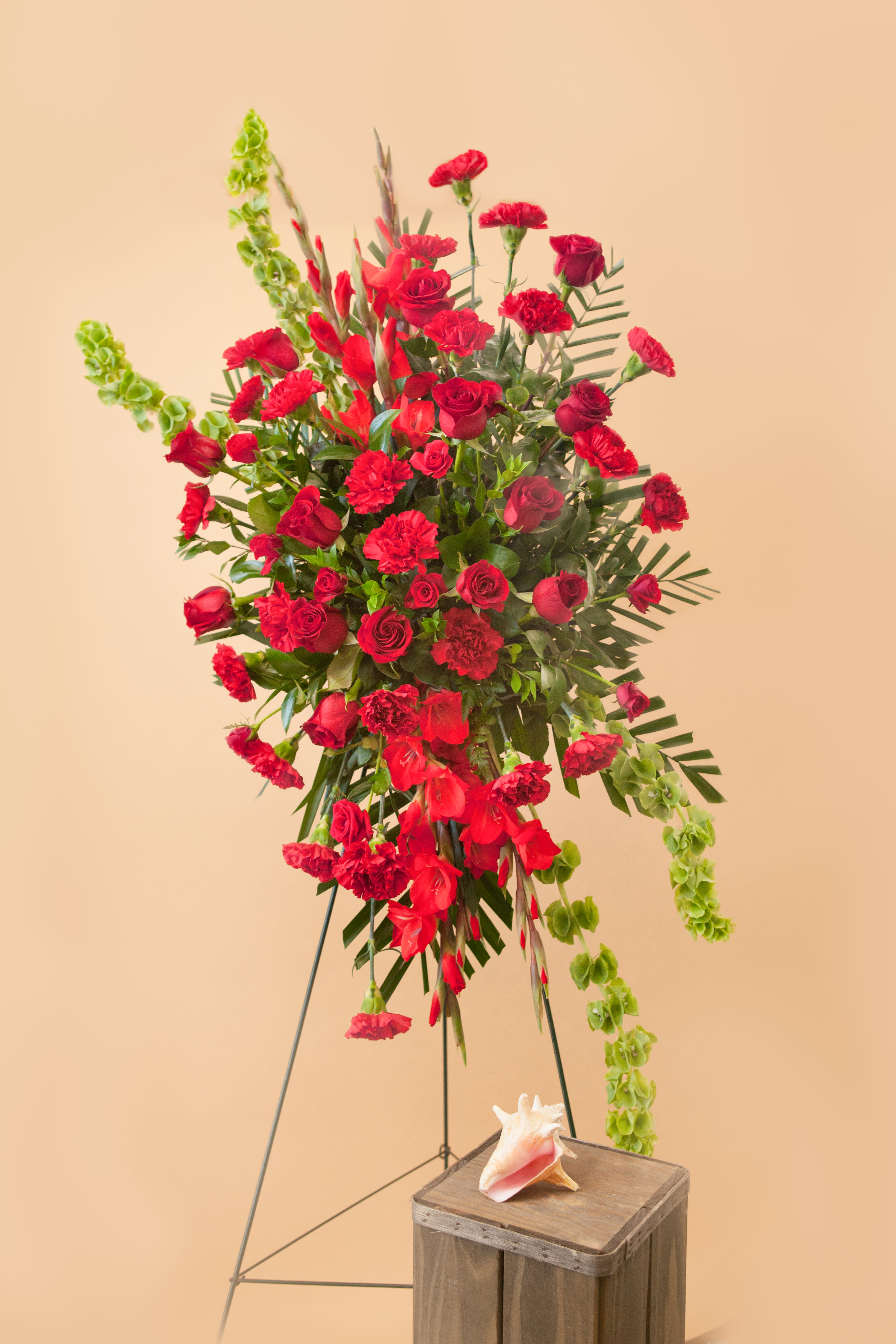 Tall red floral standing arrangement with roses and carnations on a metal easel