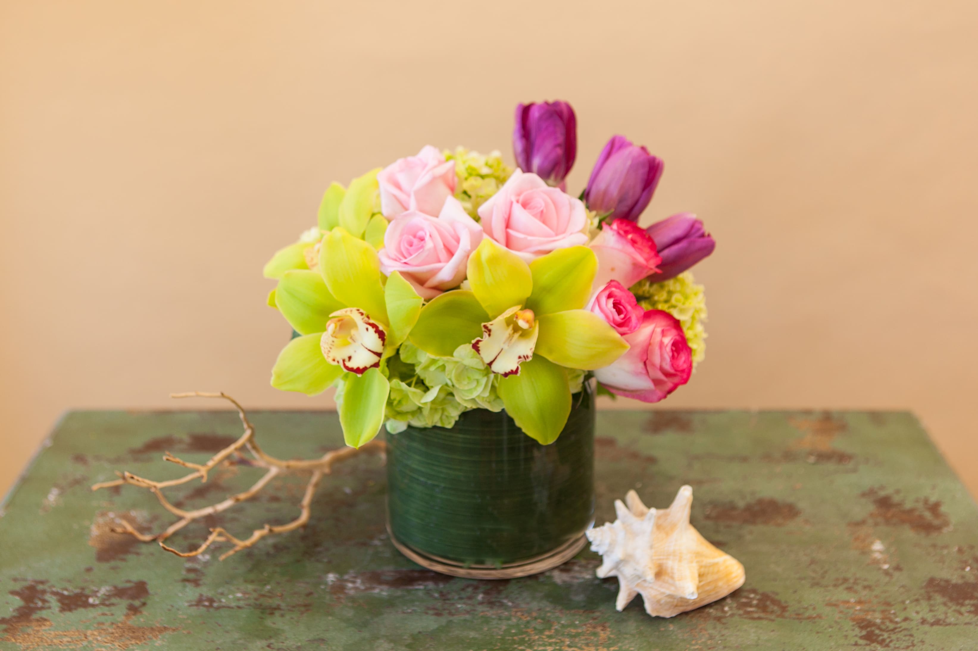 Pink roses and green orchids arranged in a dark vase