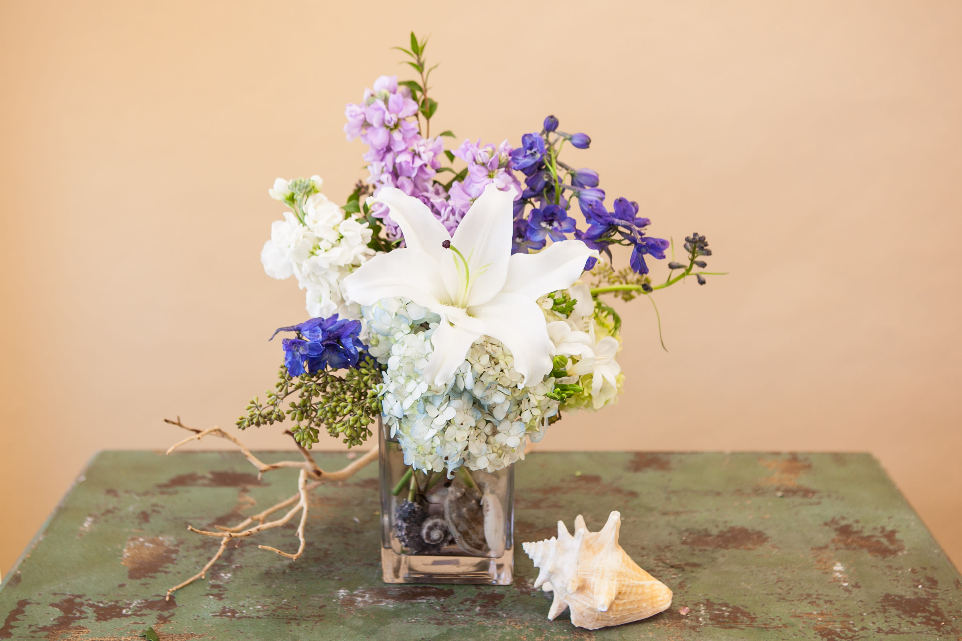 White lily bouquet with blue and lavender flowers in a glass vase