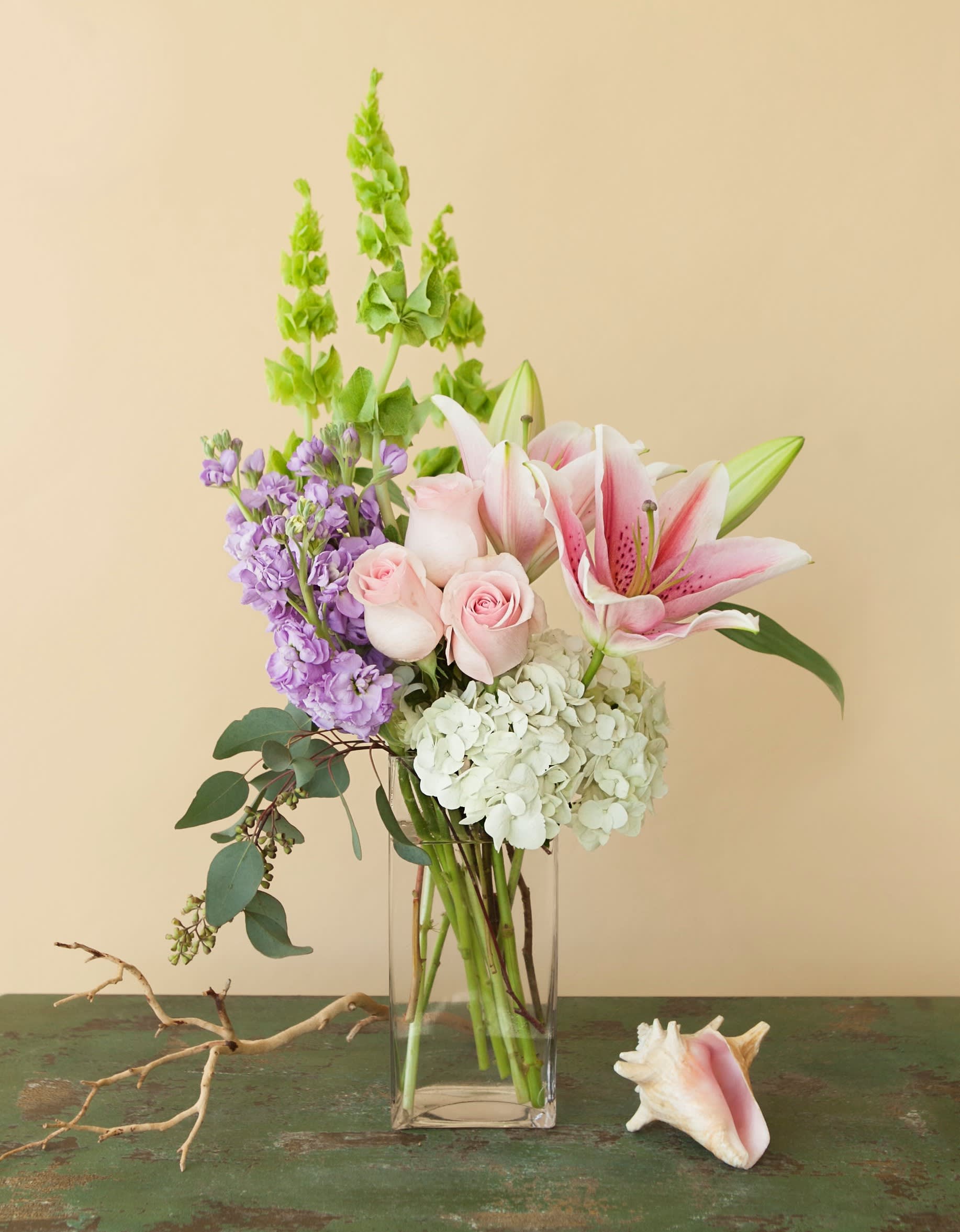 Pink lilies, roses, hydrangea, and purple stock in a glass vase