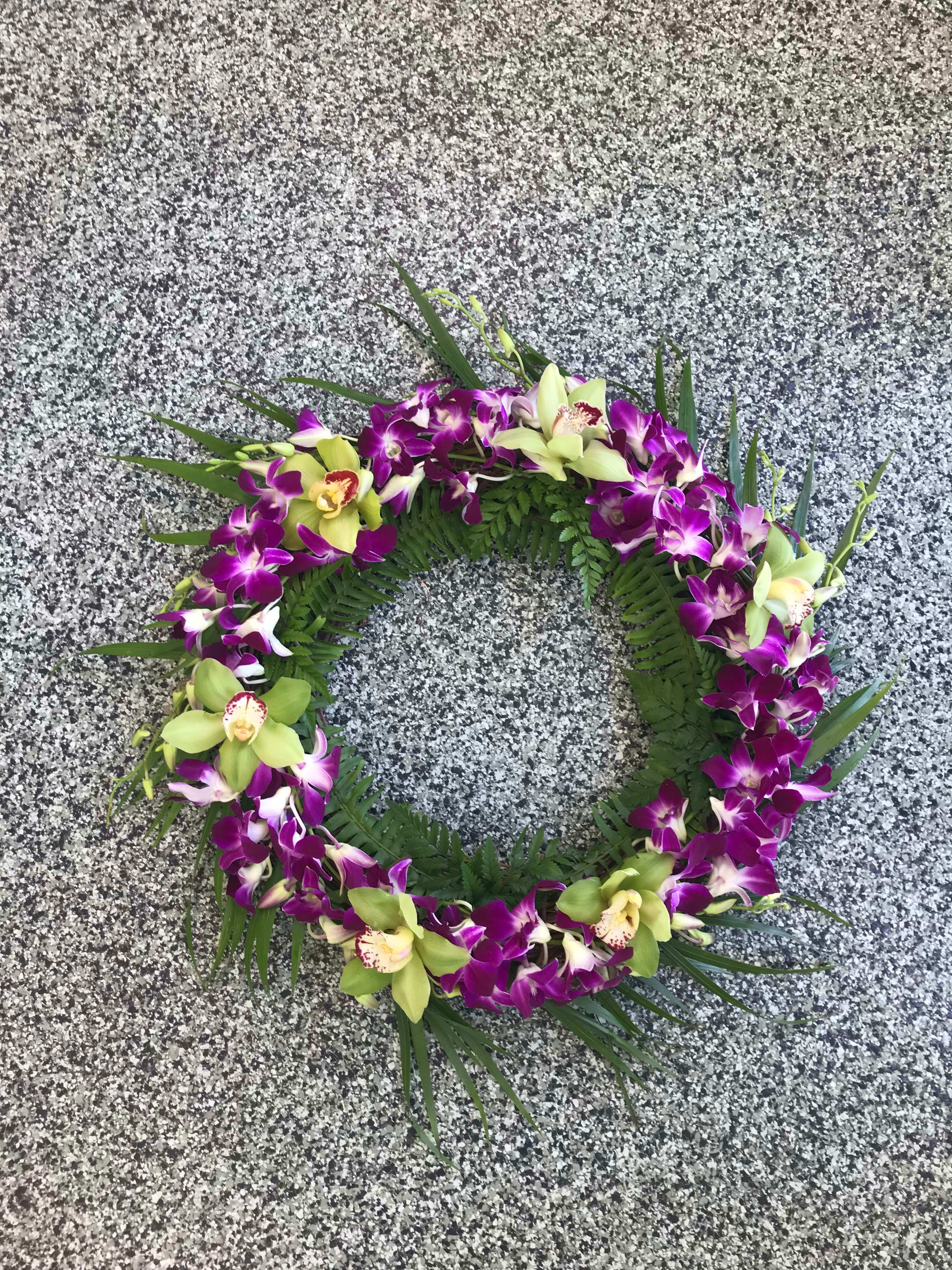 Circular orchid wreath with purple and green blooms on a stone surface