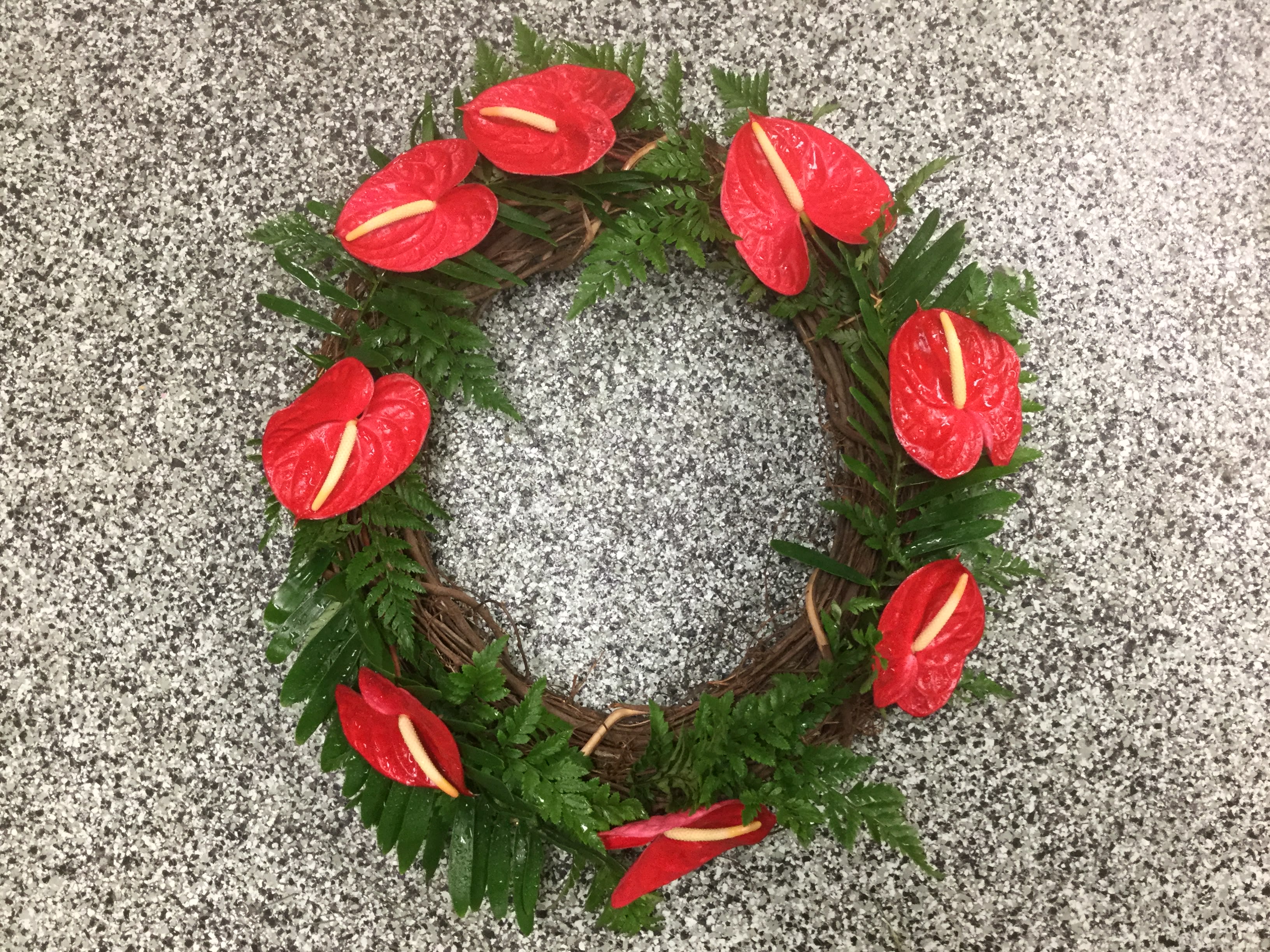 Red floral wreath with green foliage on a speckled gray surface
