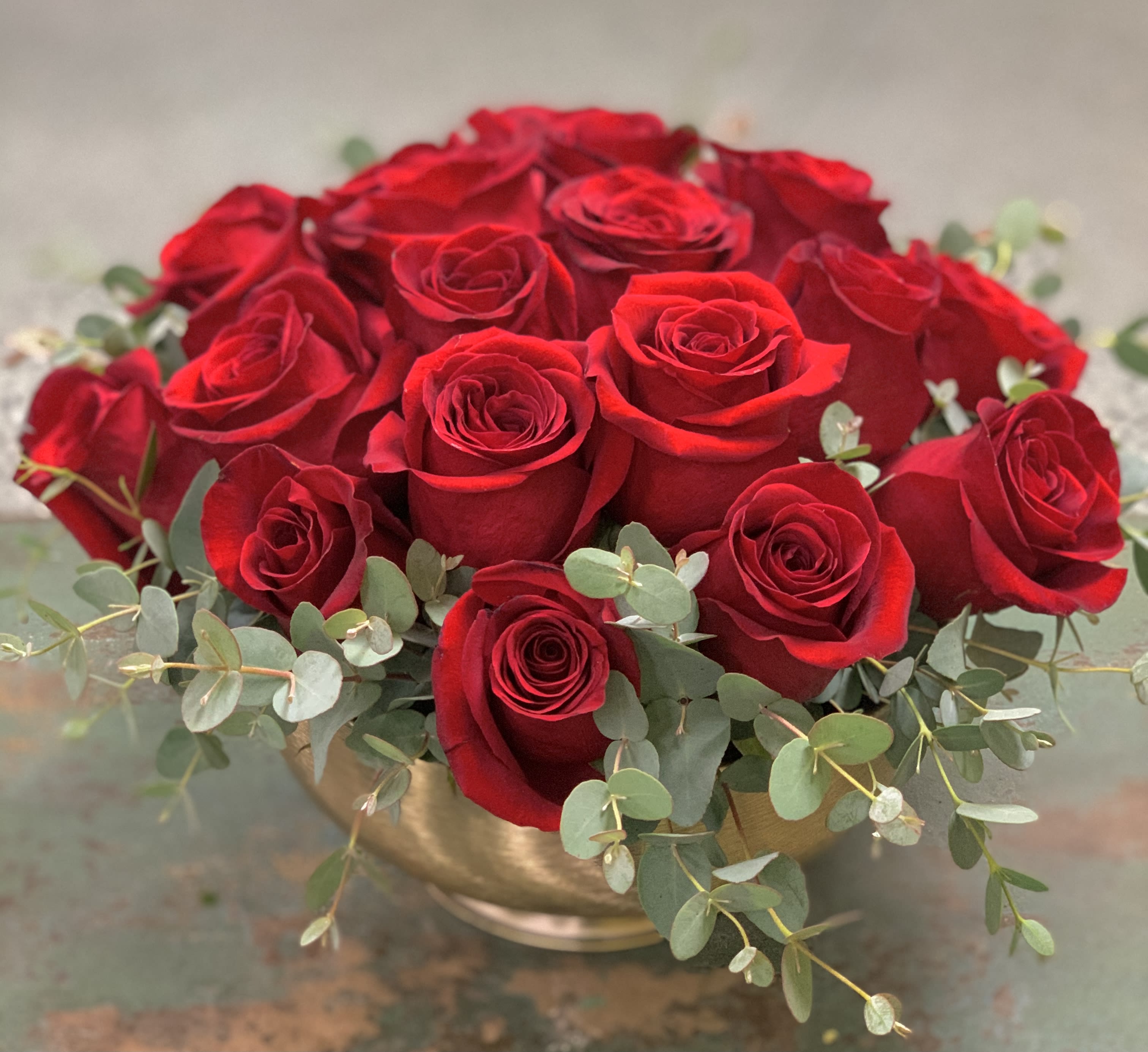 Red roses arranged in a gold bowl with eucalyptus accents