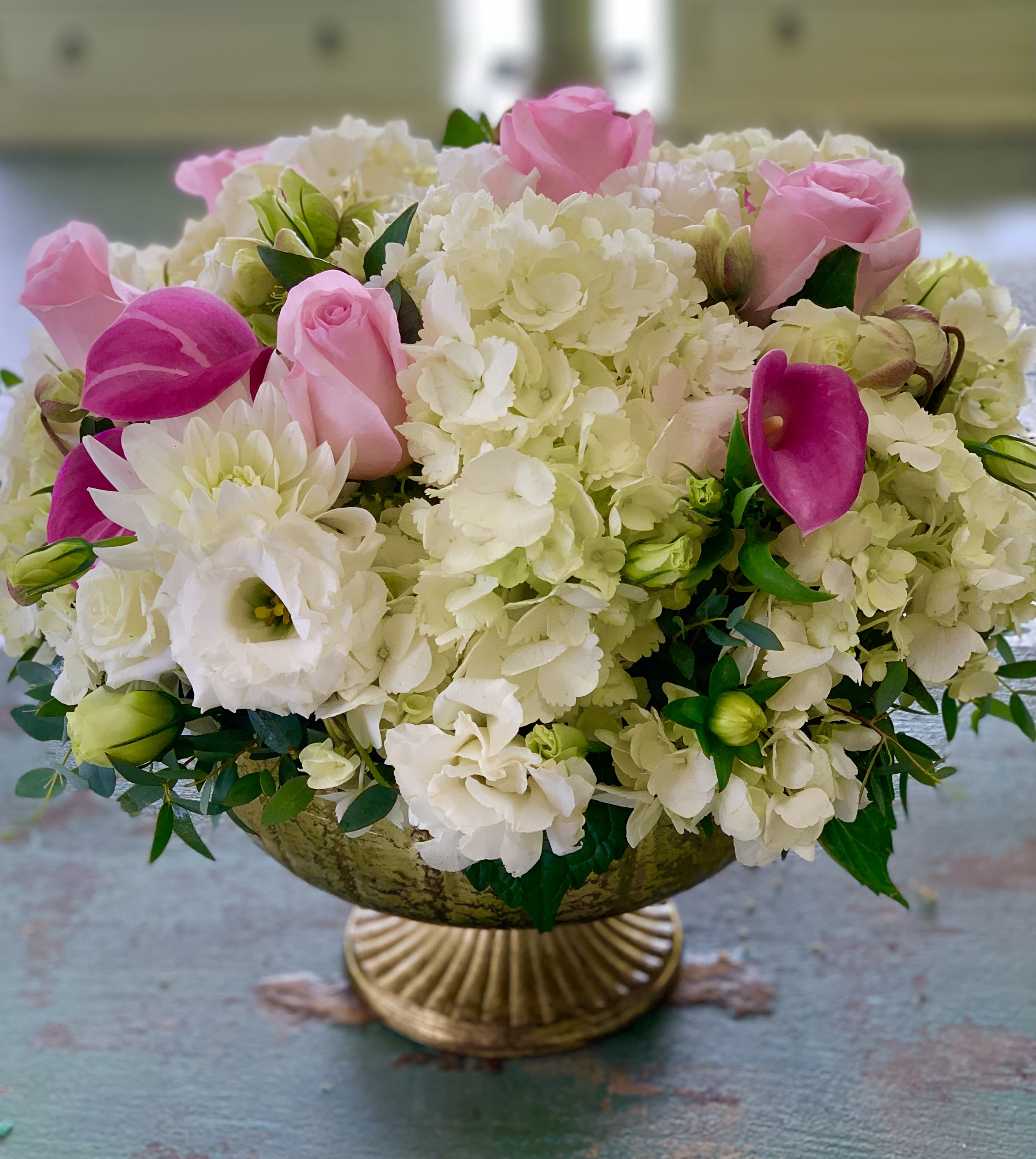 Pink roses and white hydrangeas arranged in a gold pedestal bowl