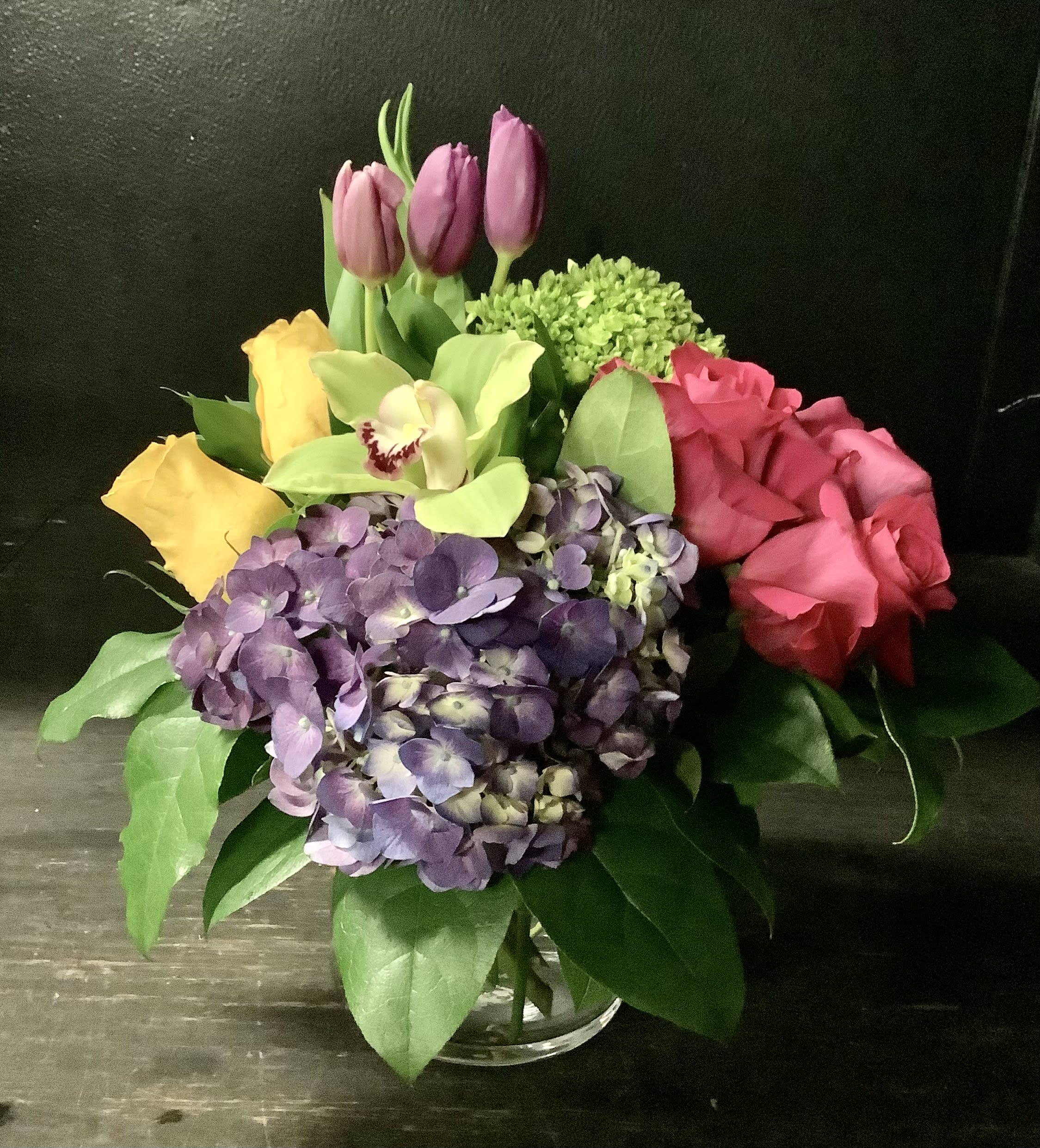 Mixed bouquet with roses, hydrangea, tulips, and orchid in a glass vase