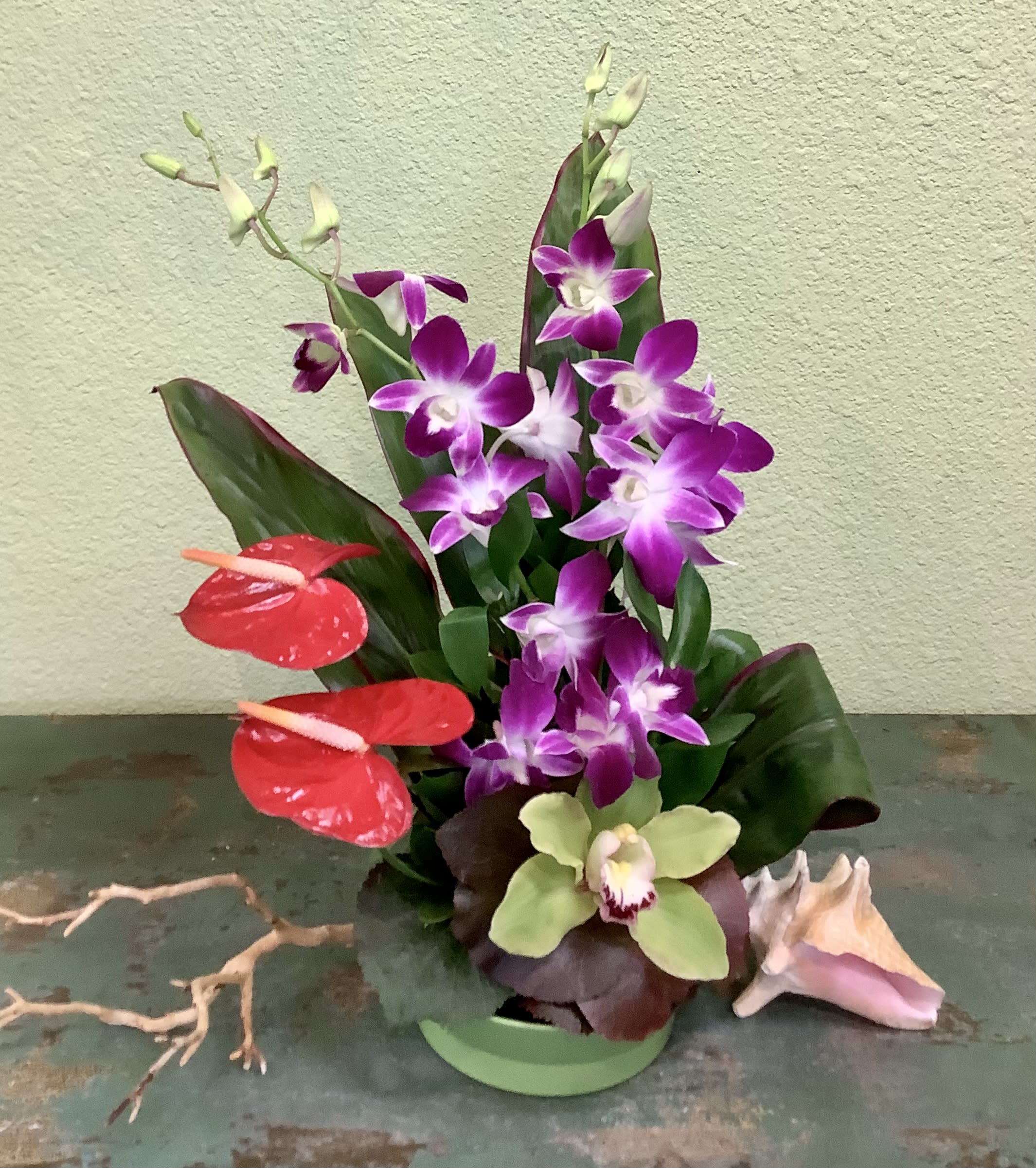 Tropical orchid arrangement in a green container with red anthuriums