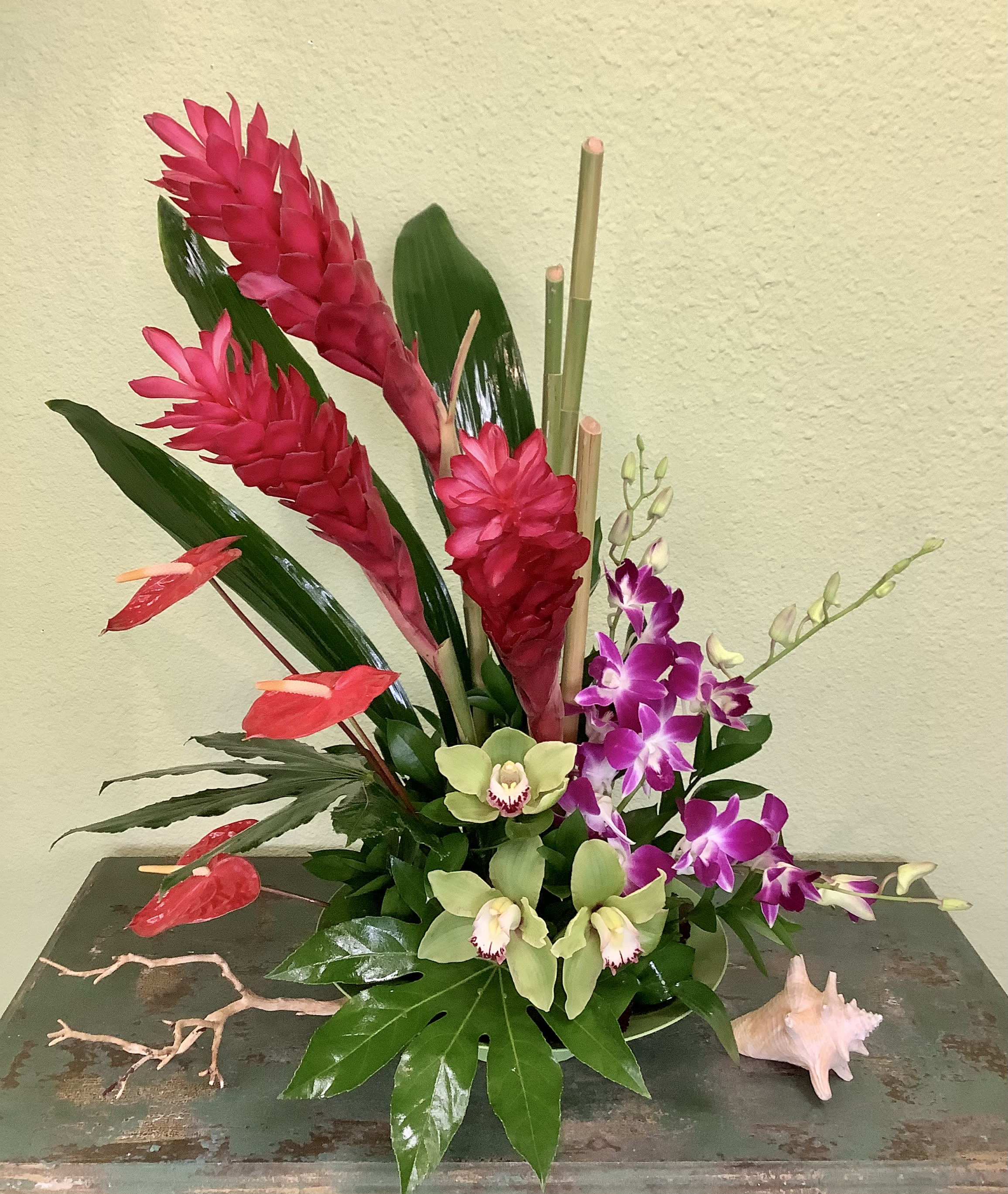 Tropical arrangement with red ginger, orchids, and anthuriums on a table