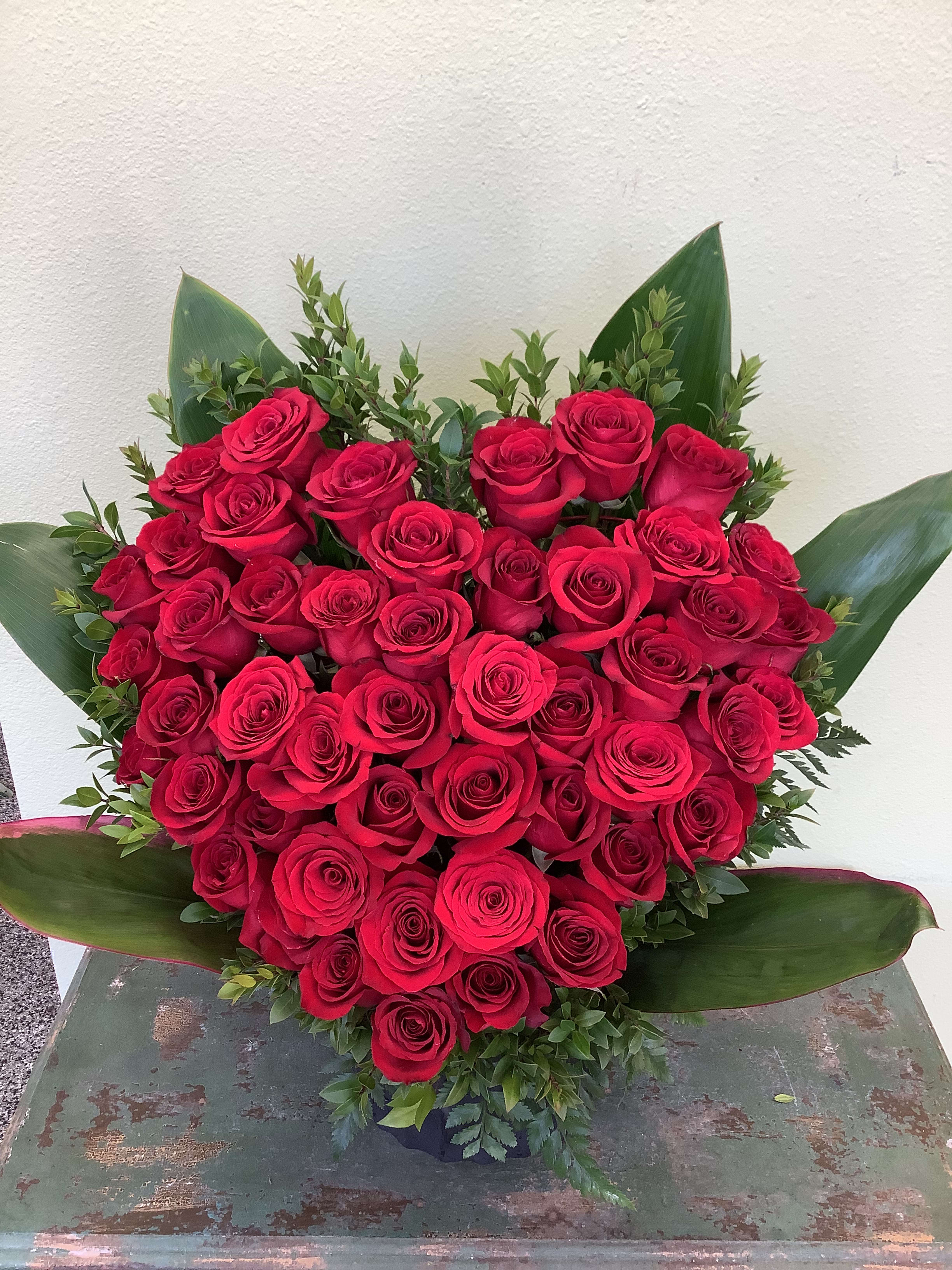 Heart-shaped bouquet of red roses with green foliage