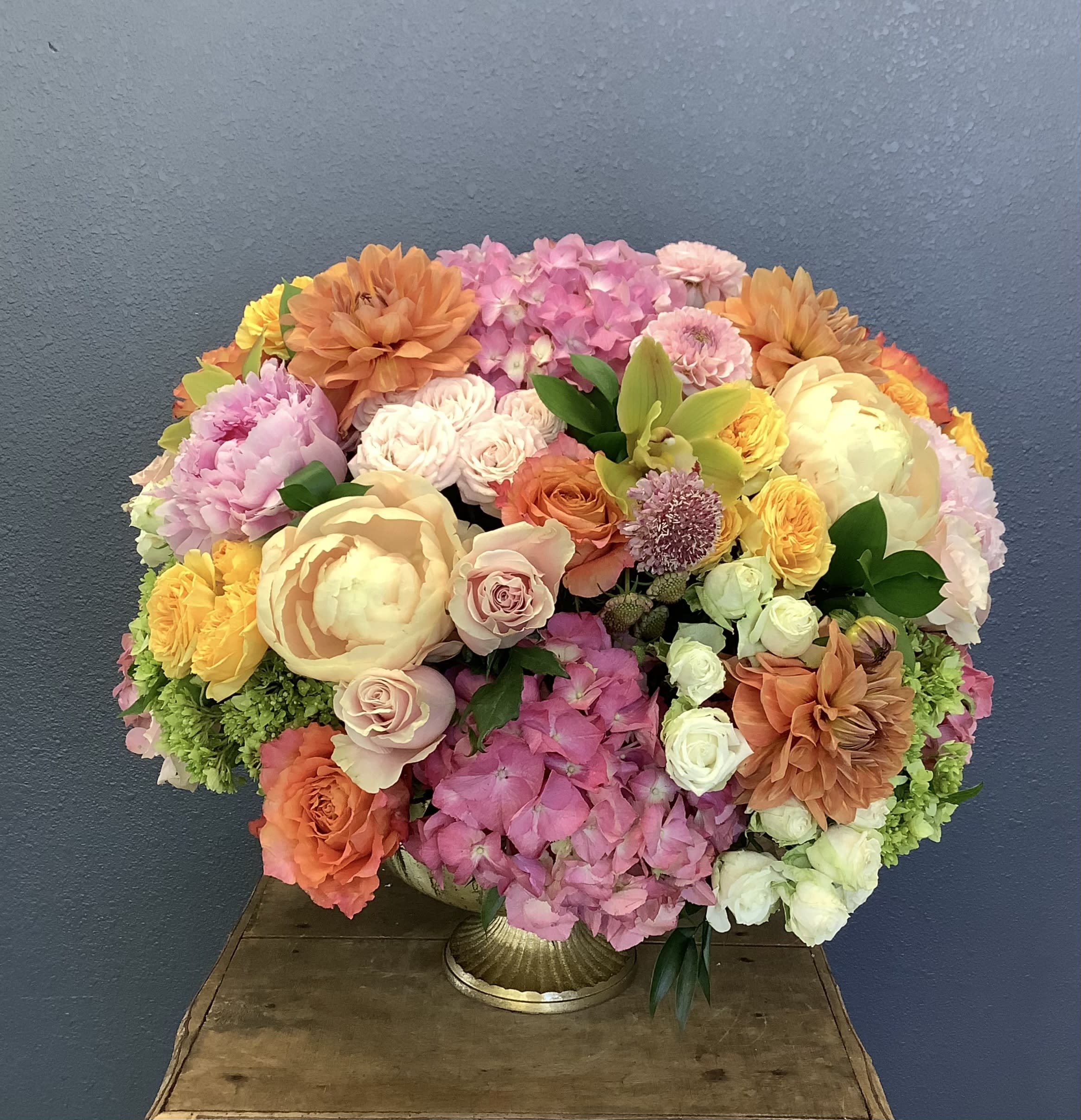Large mixed bouquet in a gold vase with pink, peach, yellow, and white blooms