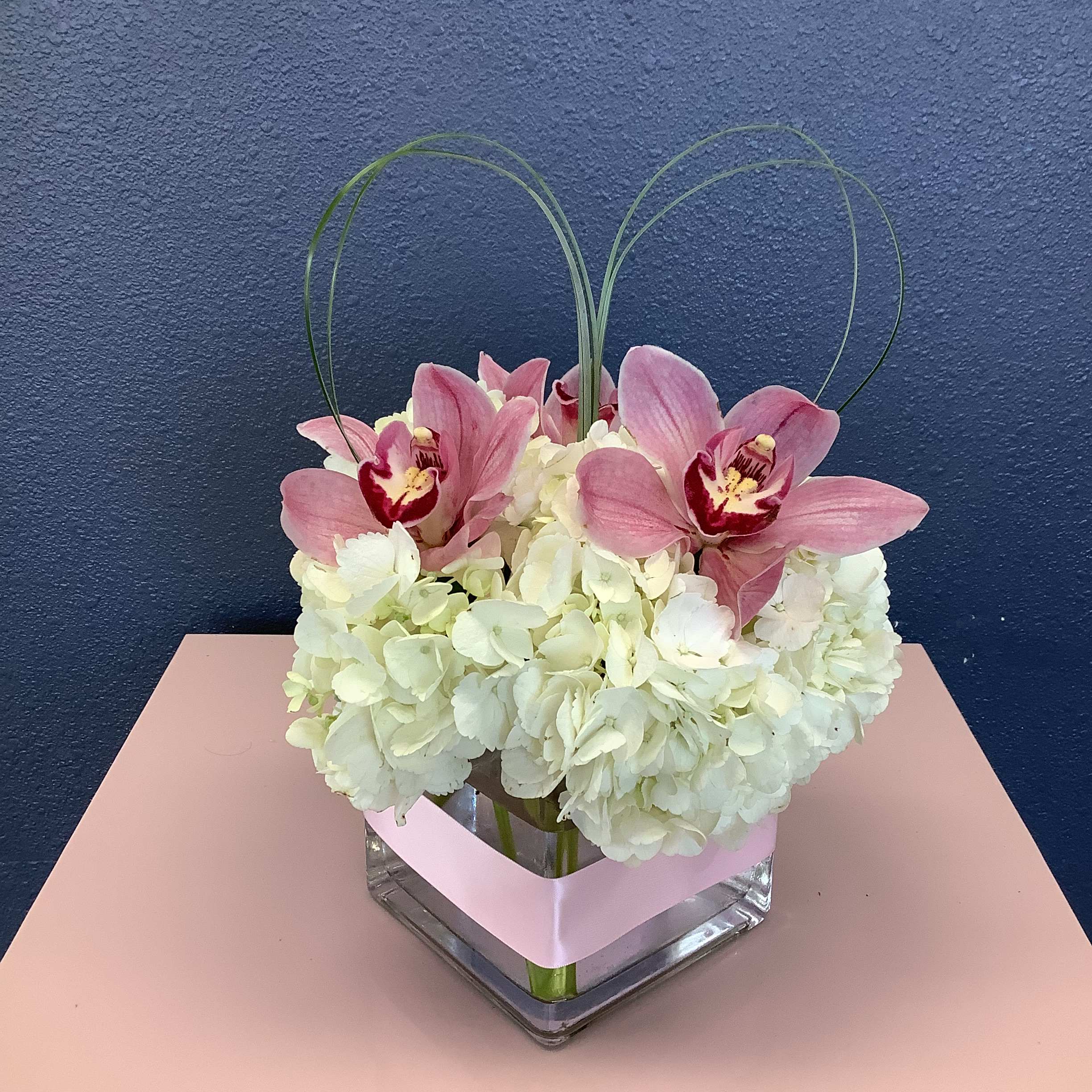 Pink orchids and white hydrangeas in a square glass vase with looped grass